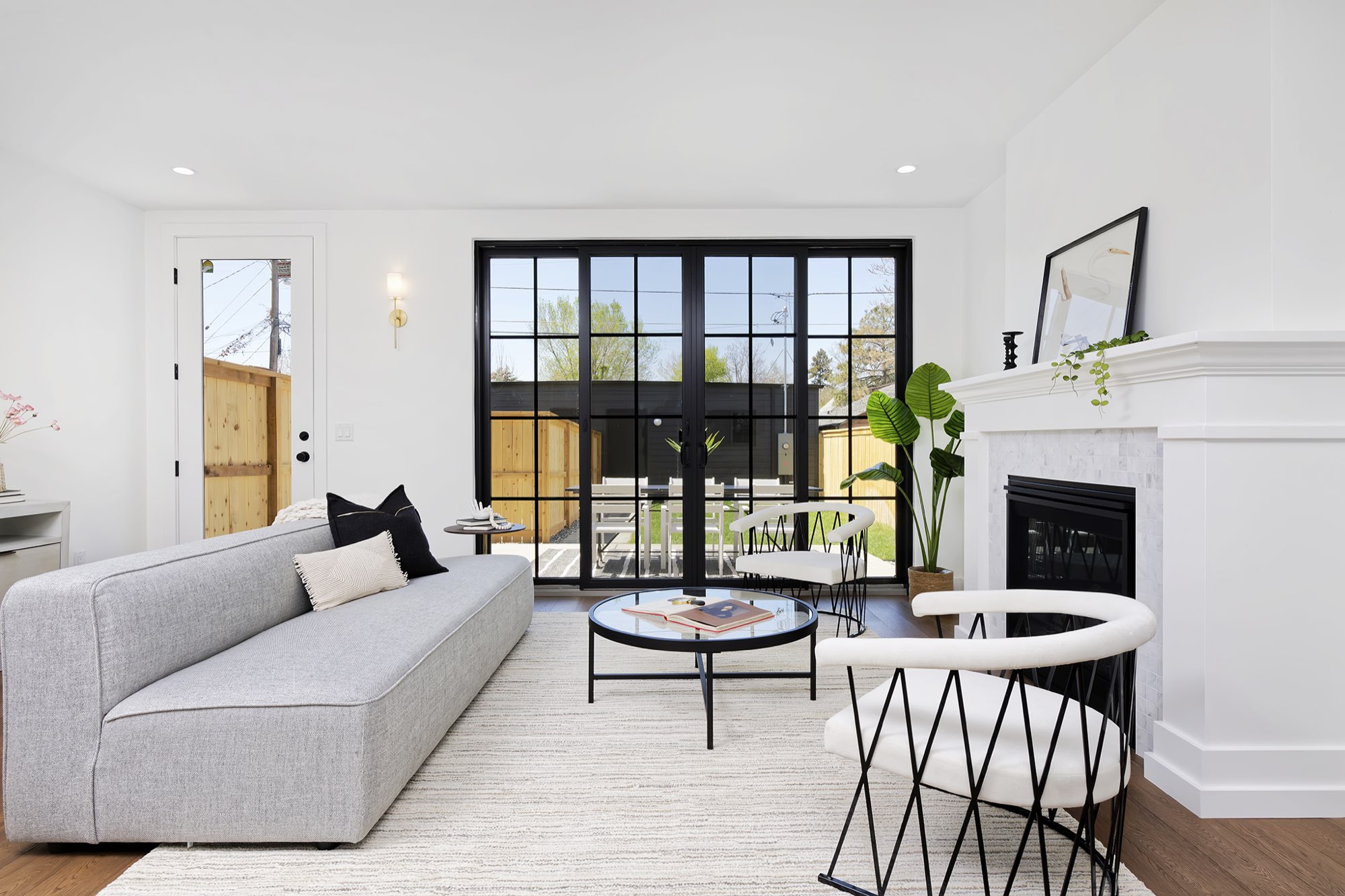 Living room with a gray sofa facing a fireplace and a wall of black-framed glass doors to the patio