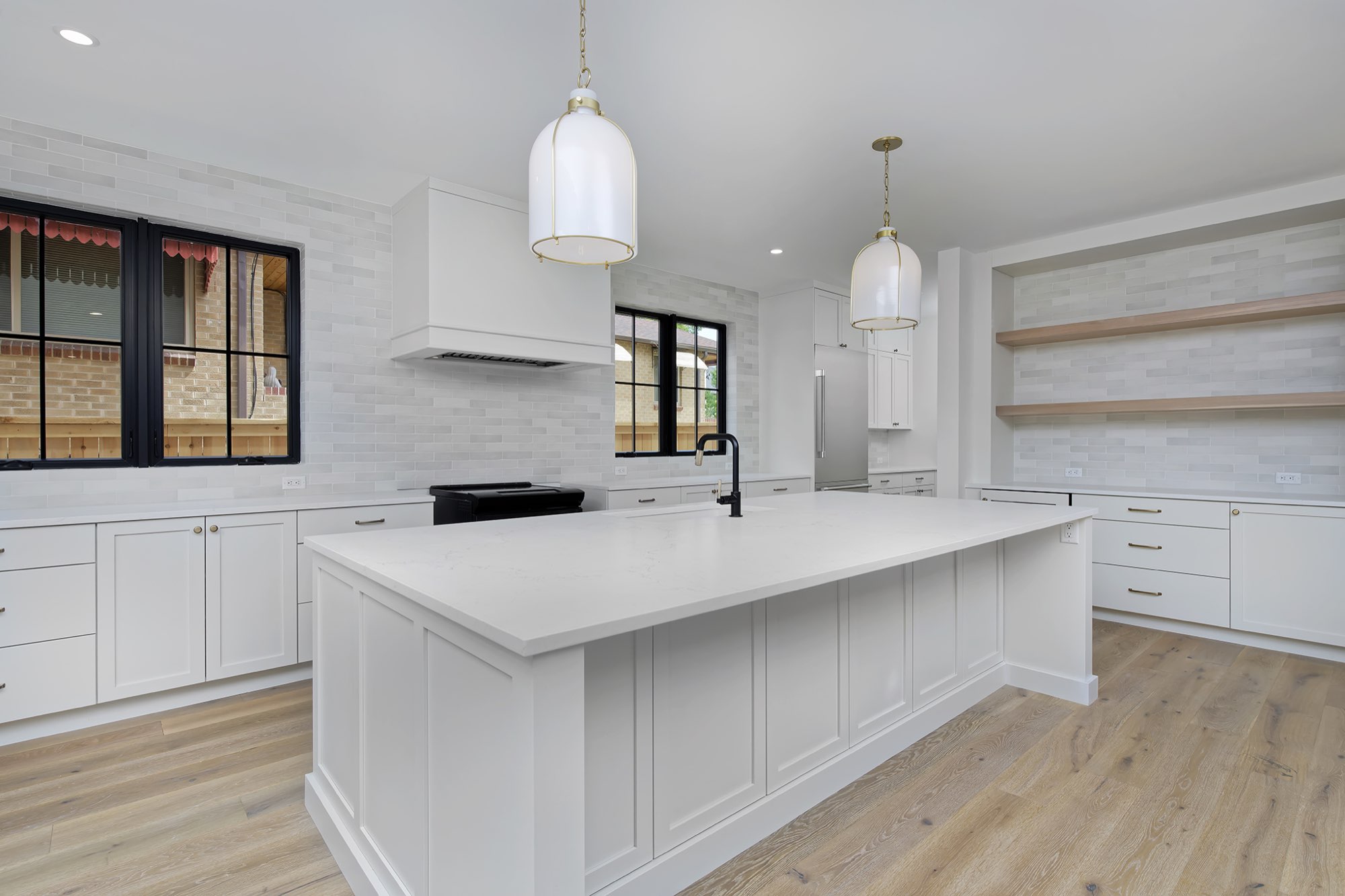 Kitchen island with a black faucet and white countertop, soft gray tile wall and brass-trimmed pendants