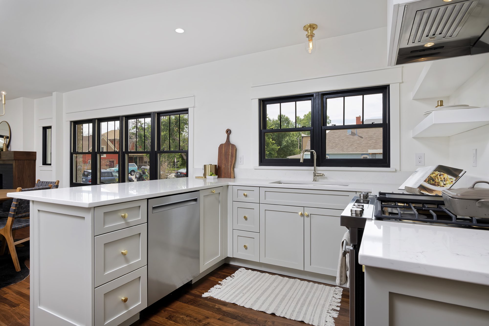 Kitchen with pale gray shaker cabinets, white counters, a stainless range and a row of black-framed windows