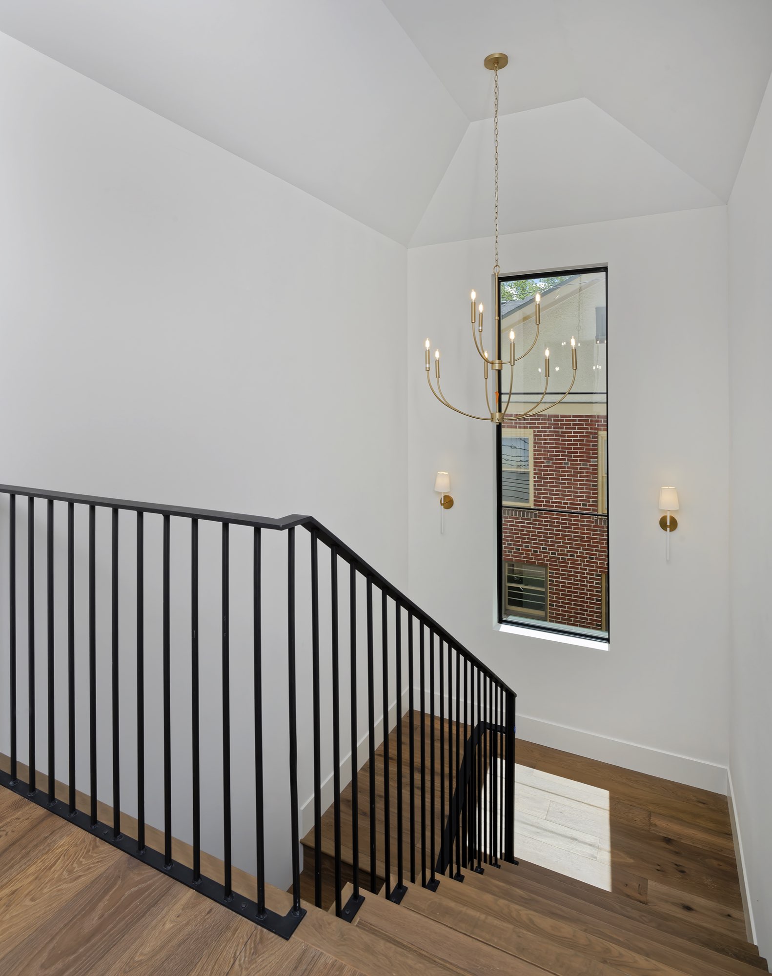 Stairwell with a black iron railing, a tall window and a brass chandelier over wood floors