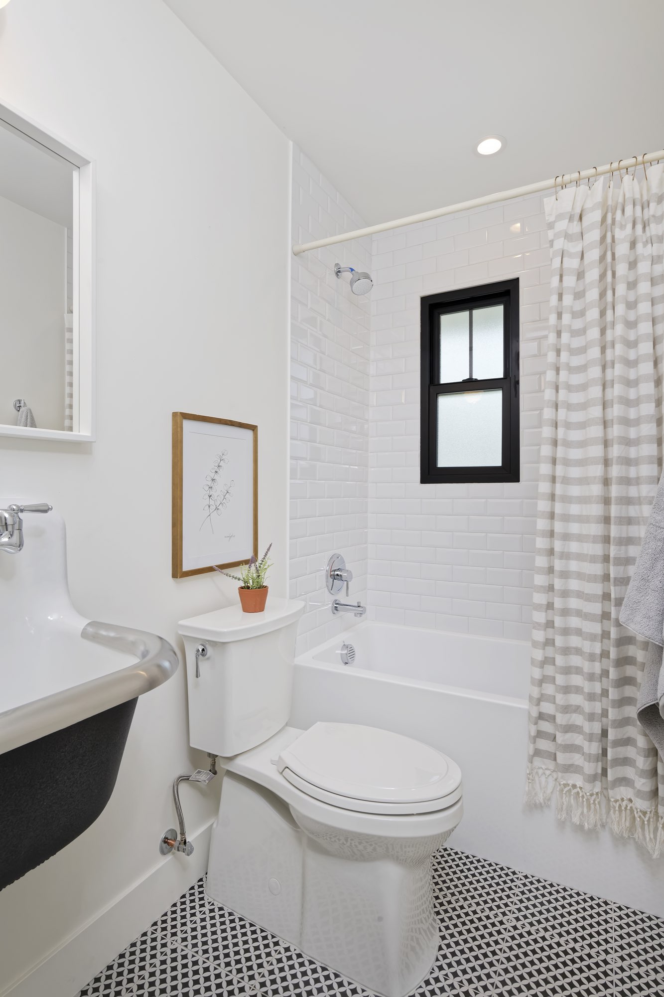 Bathroom with a wall-hung sink, toilet and tub with white subway tile on a black and white tile floor