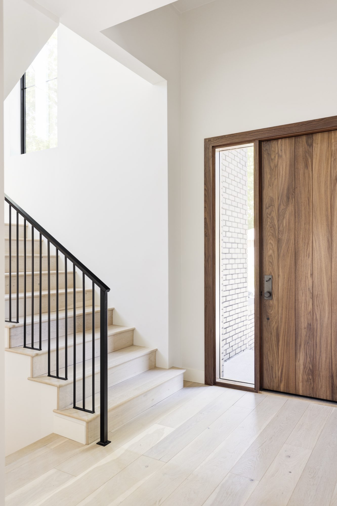 Entry with a tall wood front door and sidelight, light wide-plank floors and an open stair with a black metal railing