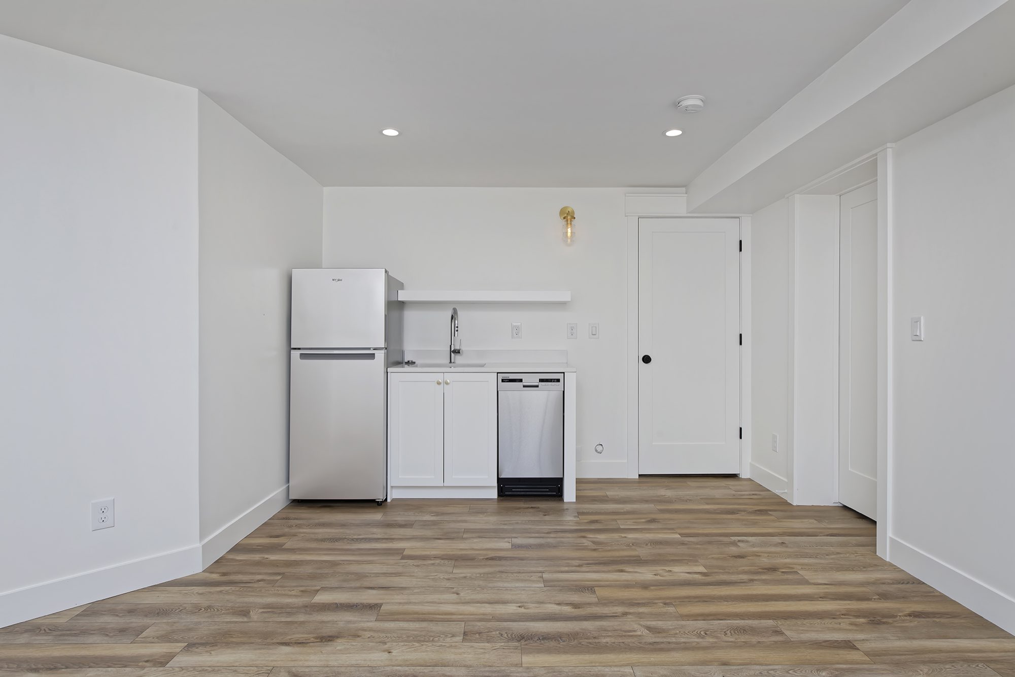 Lower-level room with a kitchenette, stainless refrigerator, white cabinets and wood-look flooring