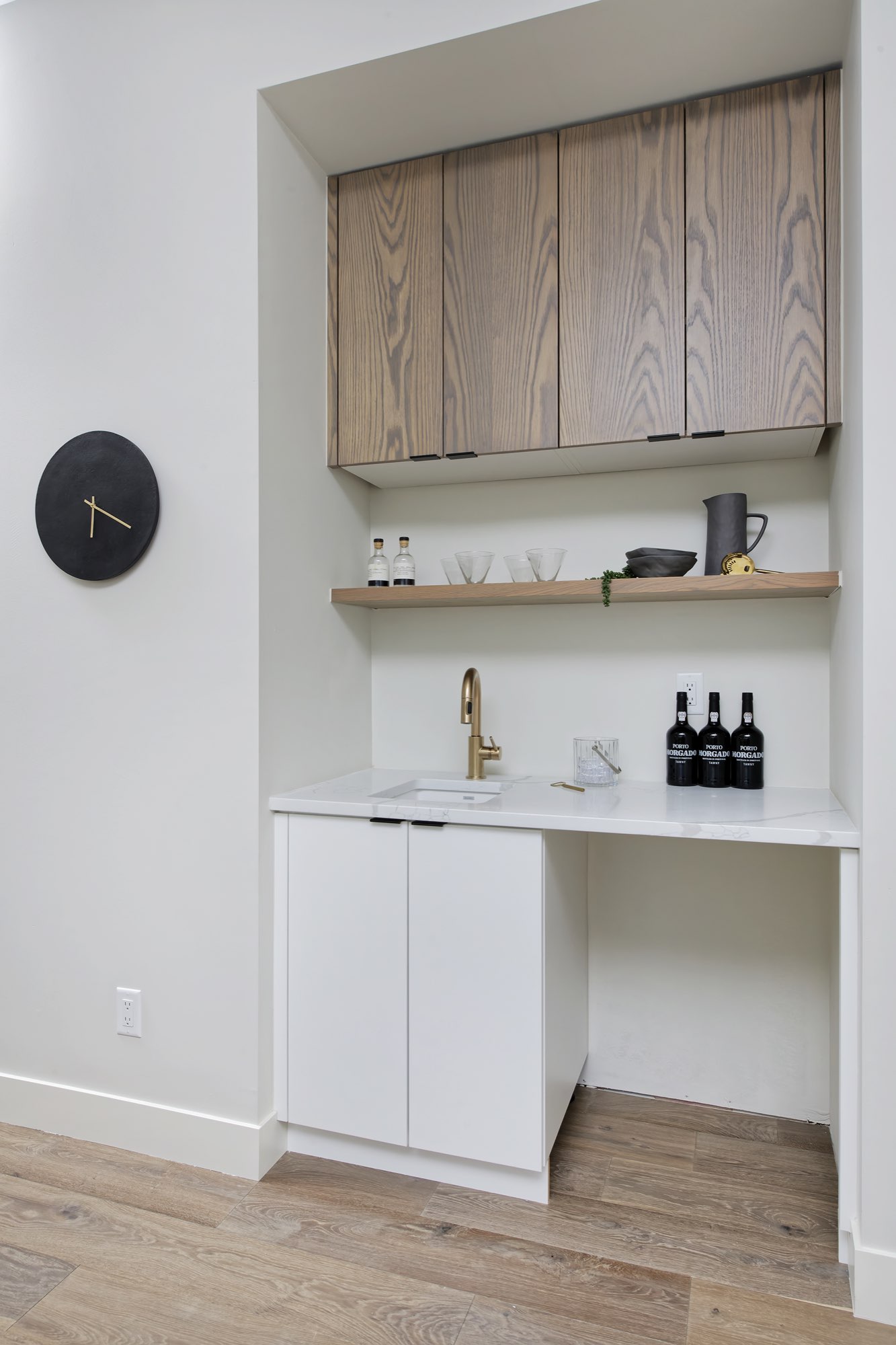 Wet bar niche with wood-tone upper cabinets, a floating shelf, a brass faucet and white lower cabinets