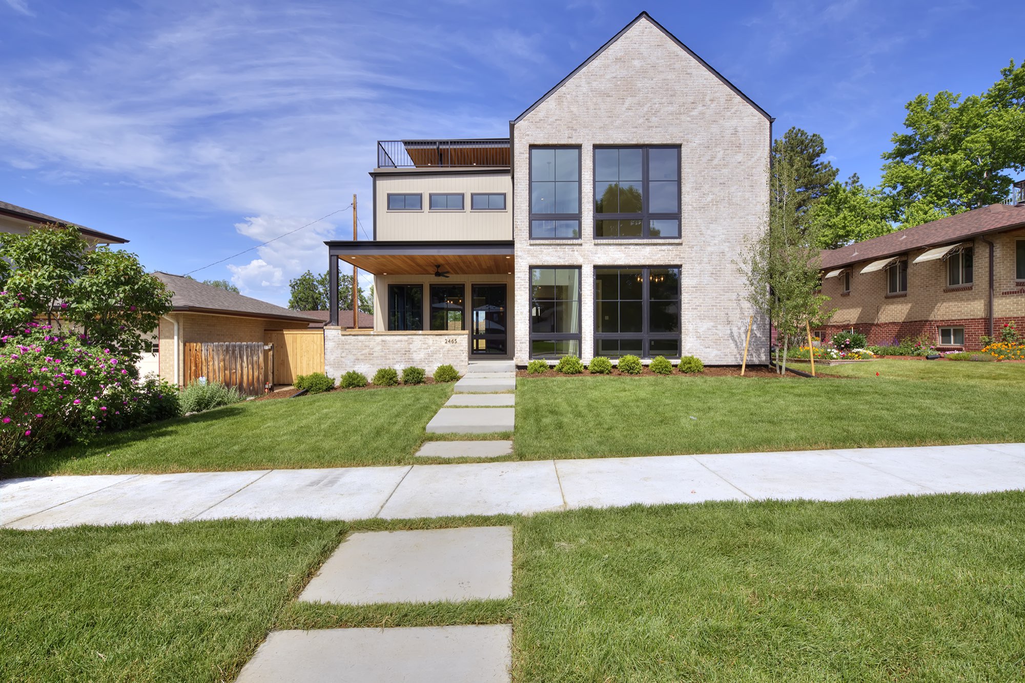 Straight-on front of the Denver custom home with a pale brick gable, tall black-framed windows, tan siding and a covered porch