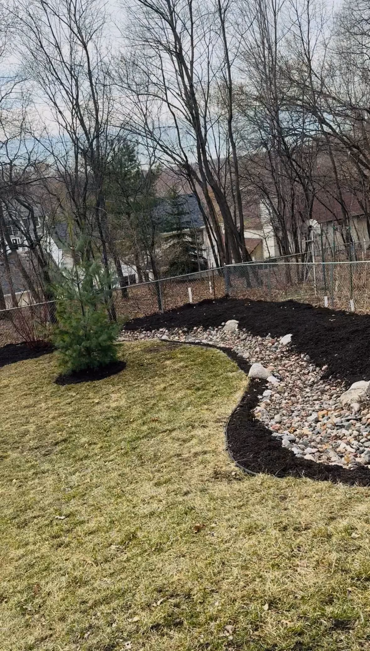 Fresh Mulch, River Rocks, and Young Trees Planted in One Backyard