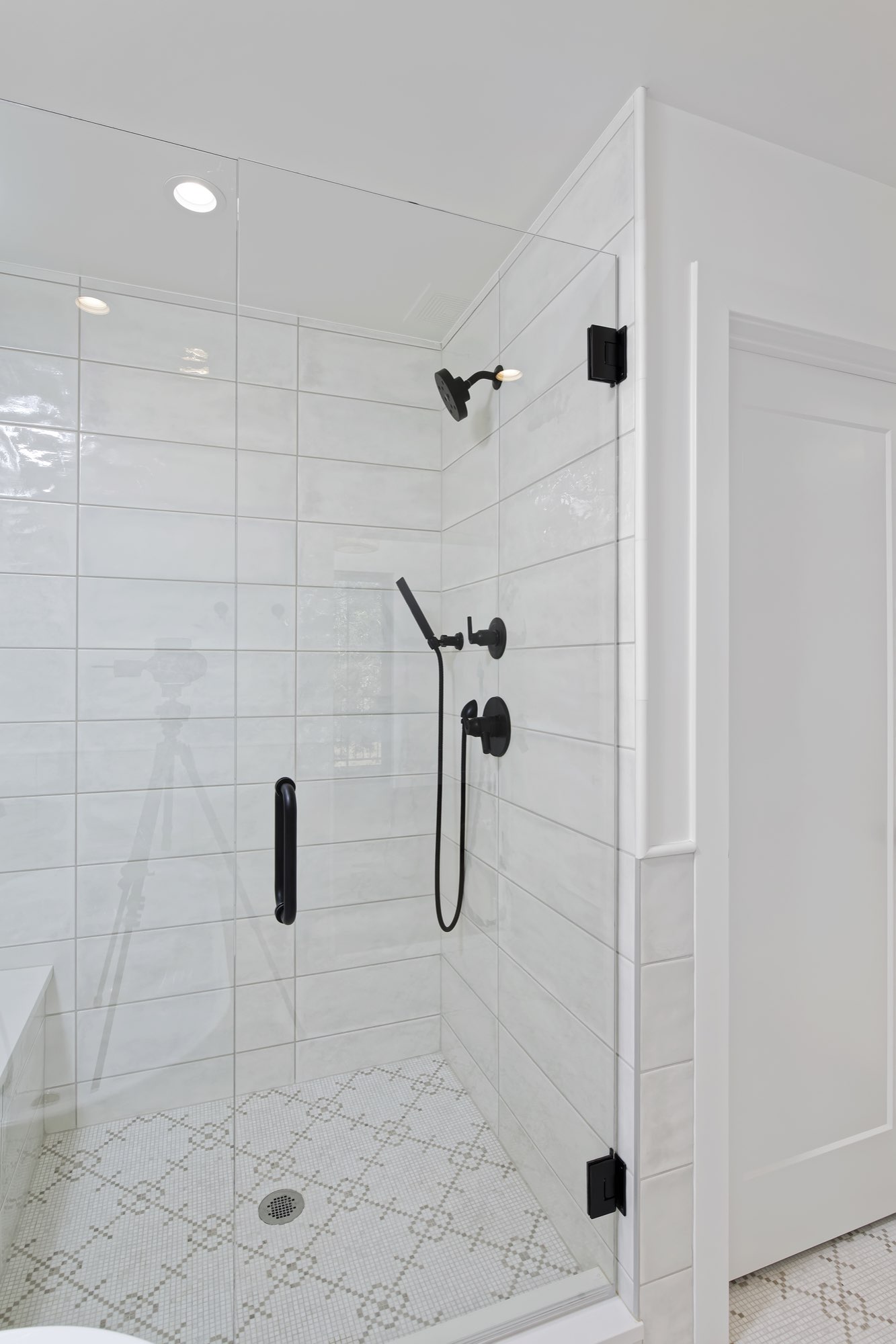 Glass shower with soft gray tile, black fixtures and a patterned mosaic floor