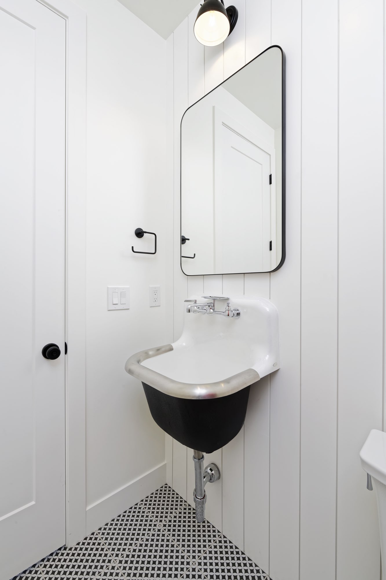 Powder room with a black wall-hung sink, rounded black mirror and white vertical paneling