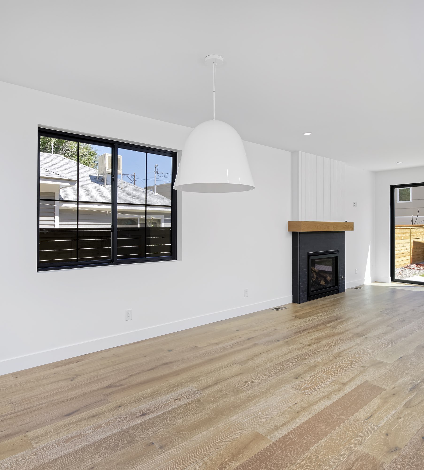 Open living and dining space with a large white dome pendant, black-framed windows, a corner fireplace and light wood floors
