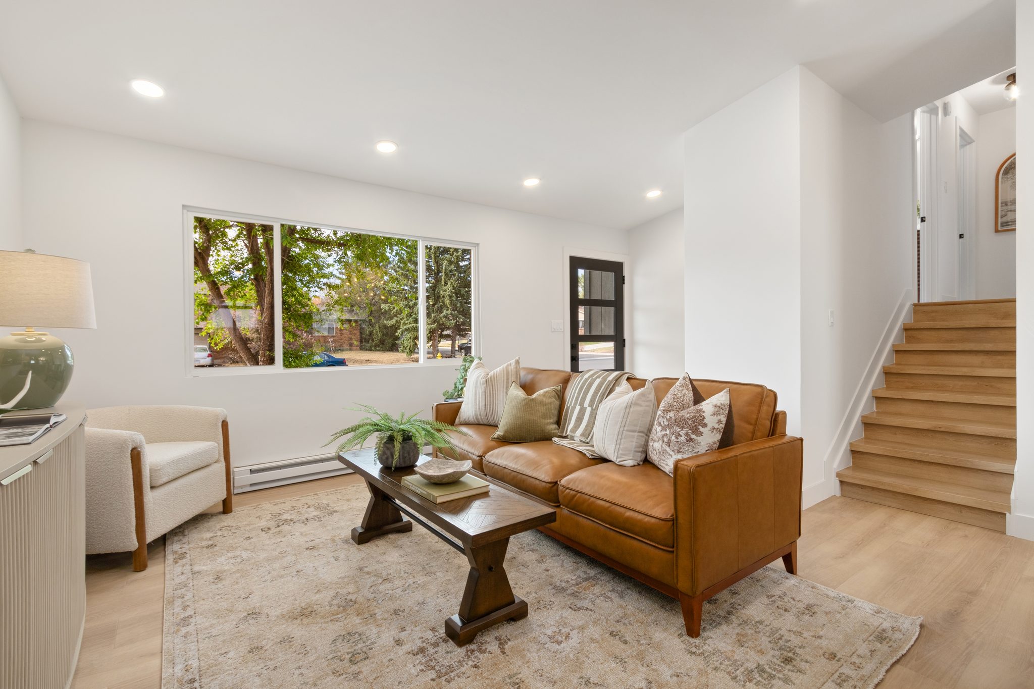 Living room with a leather sofa, a big window and the stairs leading up