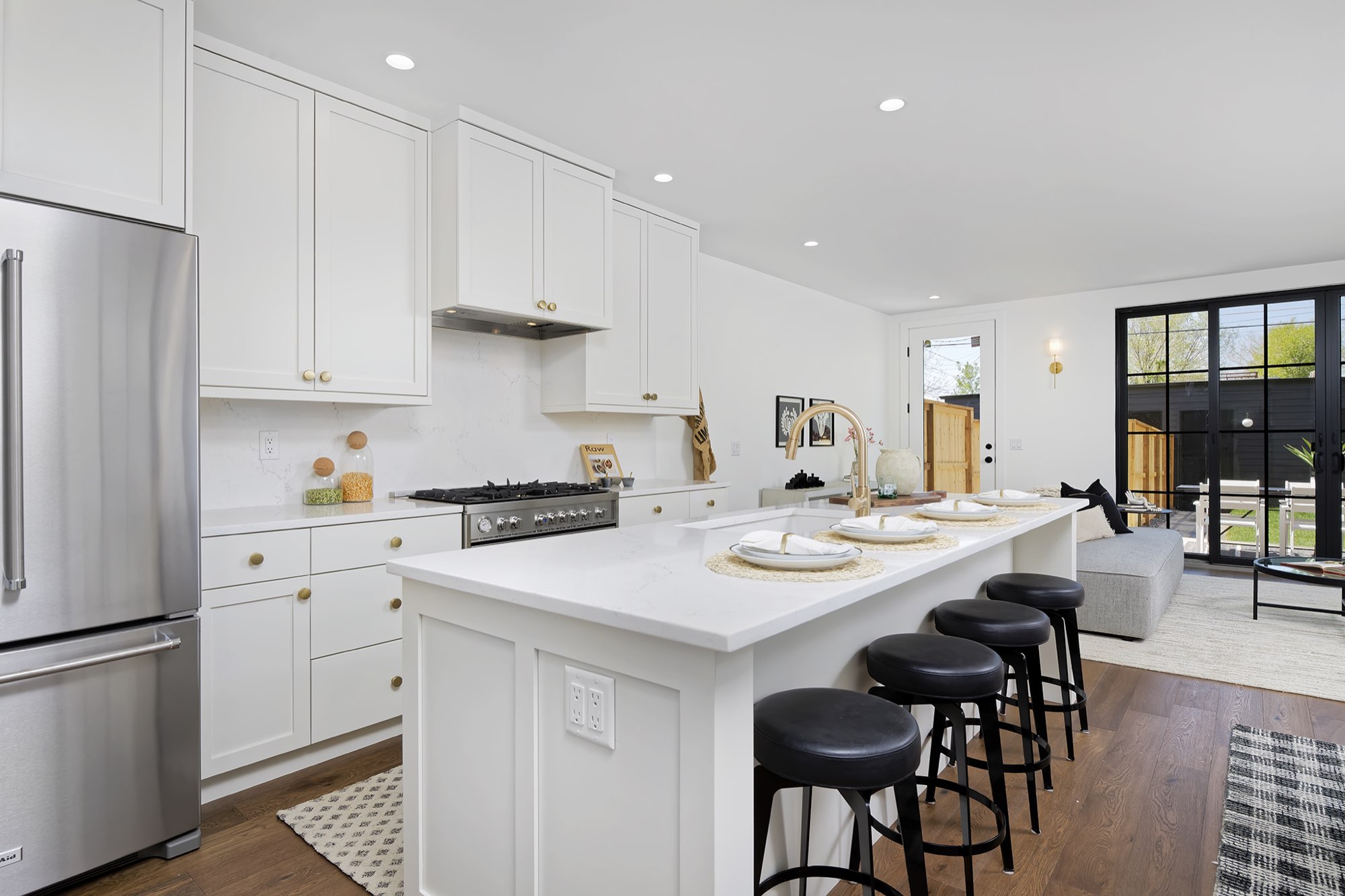 Kitchen seen across the island toward the living room, with white cabinets, a range and black-framed glass doors