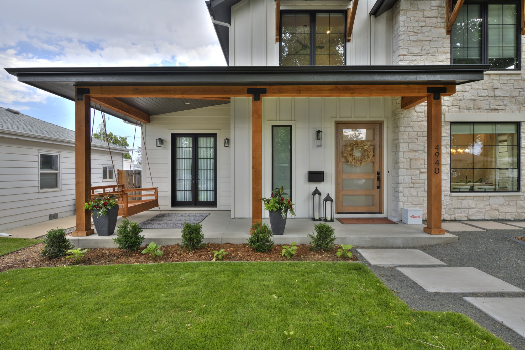 Covered front porch with timber posts, a wood front door, black-framed double doors and a porch swing