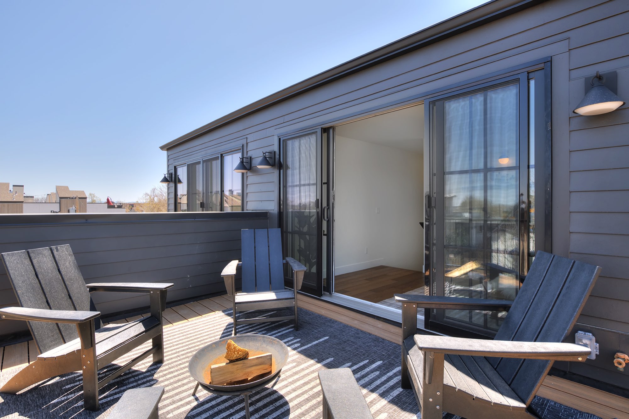 Rooftop deck with chairs and a fire bowl along the dark siding wall and glass doors
