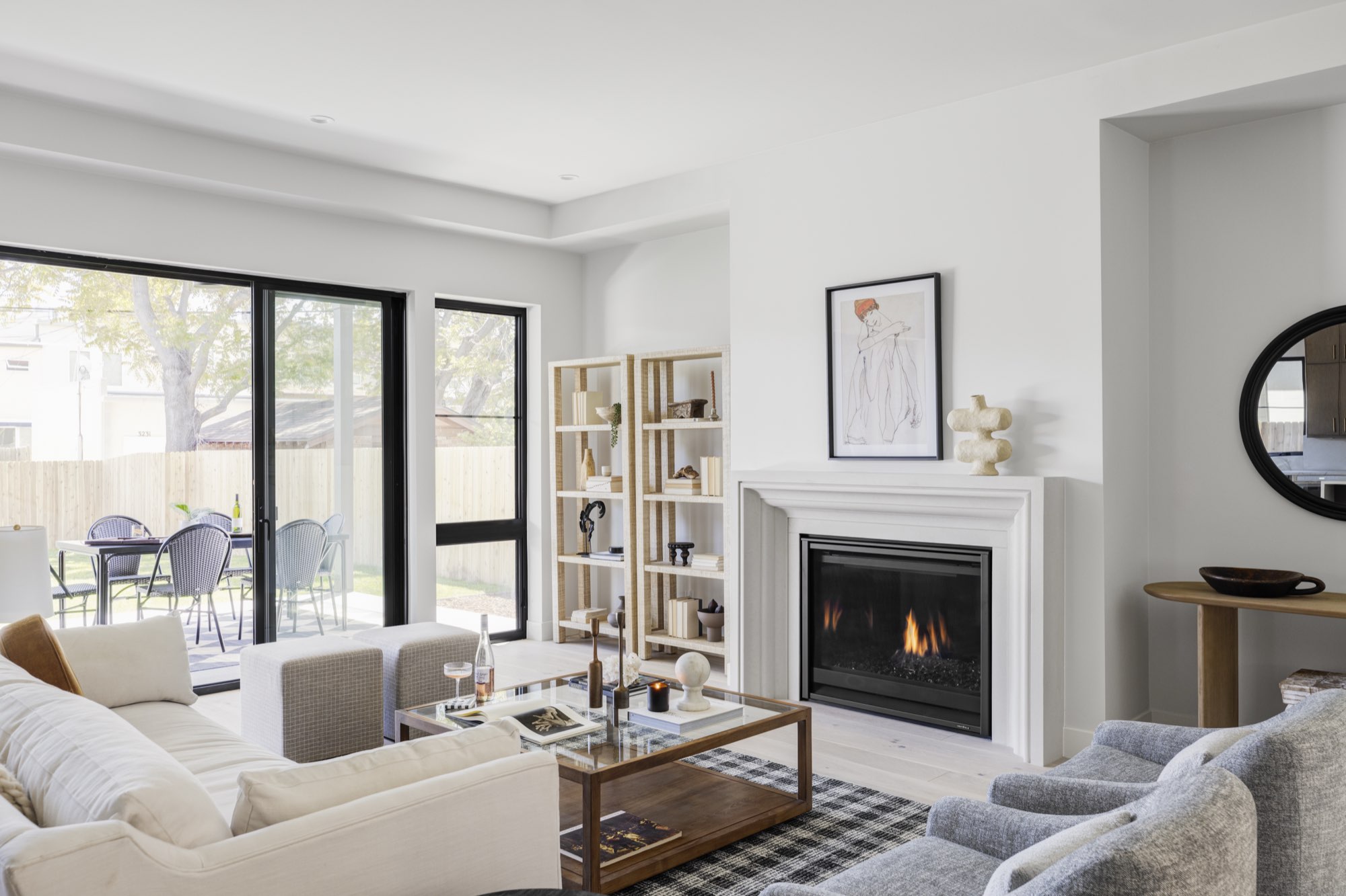 Living room with a white fireplace, black-framed sliding doors to the patio and light wide-plank wood floors