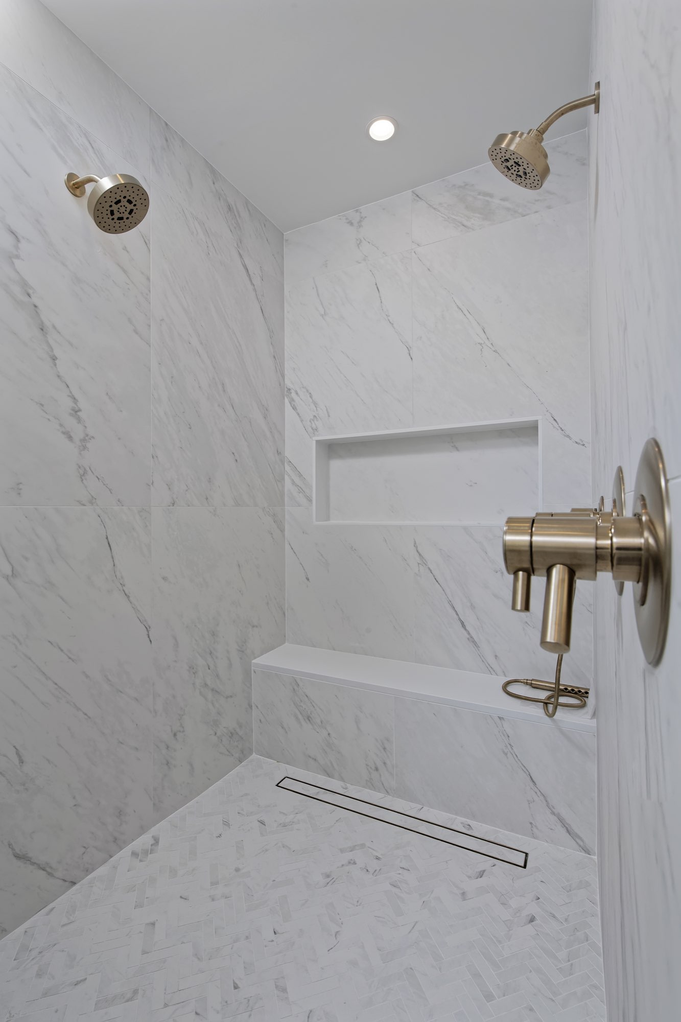 Walk-in shower in white veined stone with a brass shower fixture and a linear drain