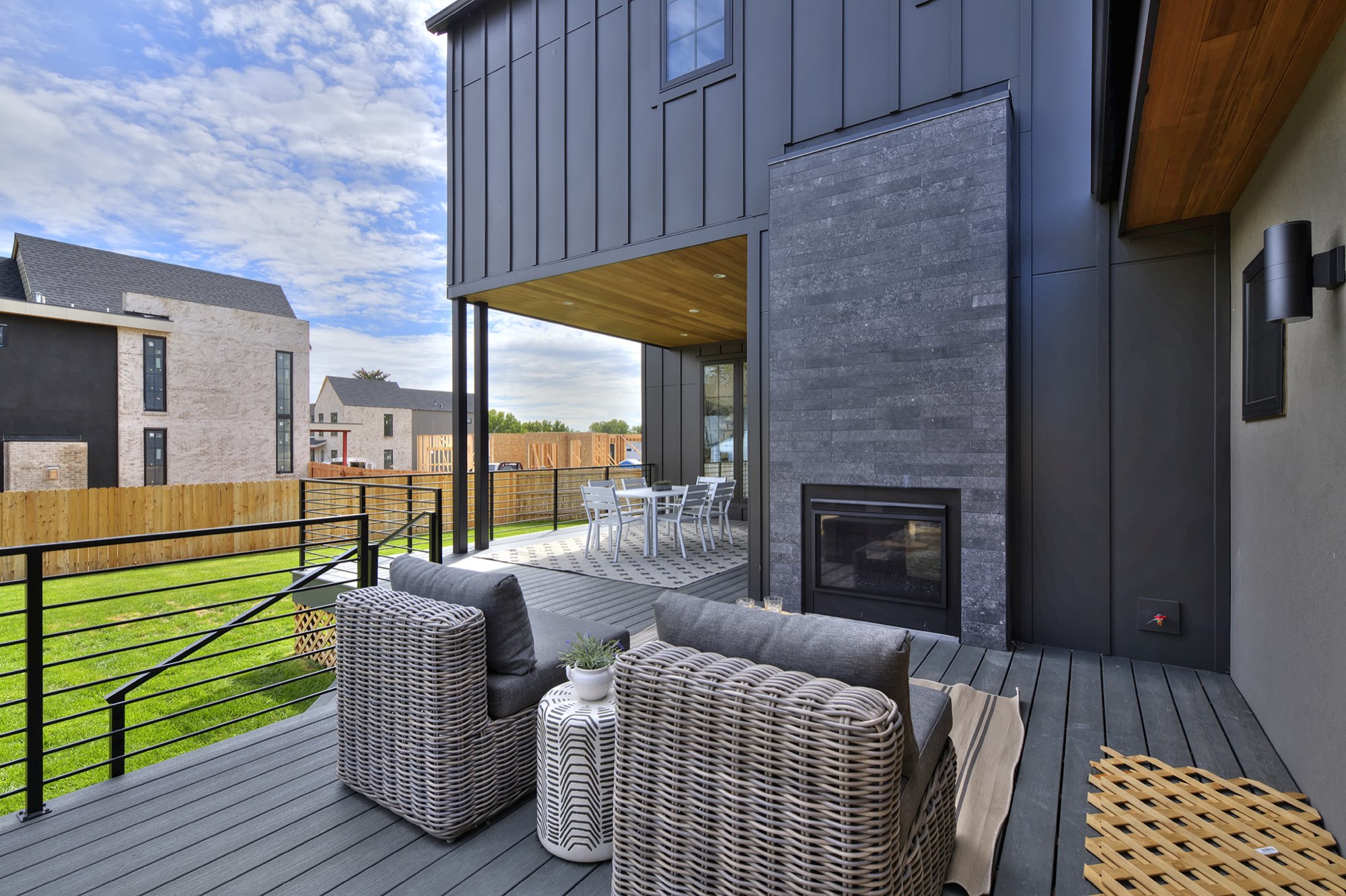 Outdoor stone fireplace on the covered deck wall with two wicker chairs and a black horizontal railing