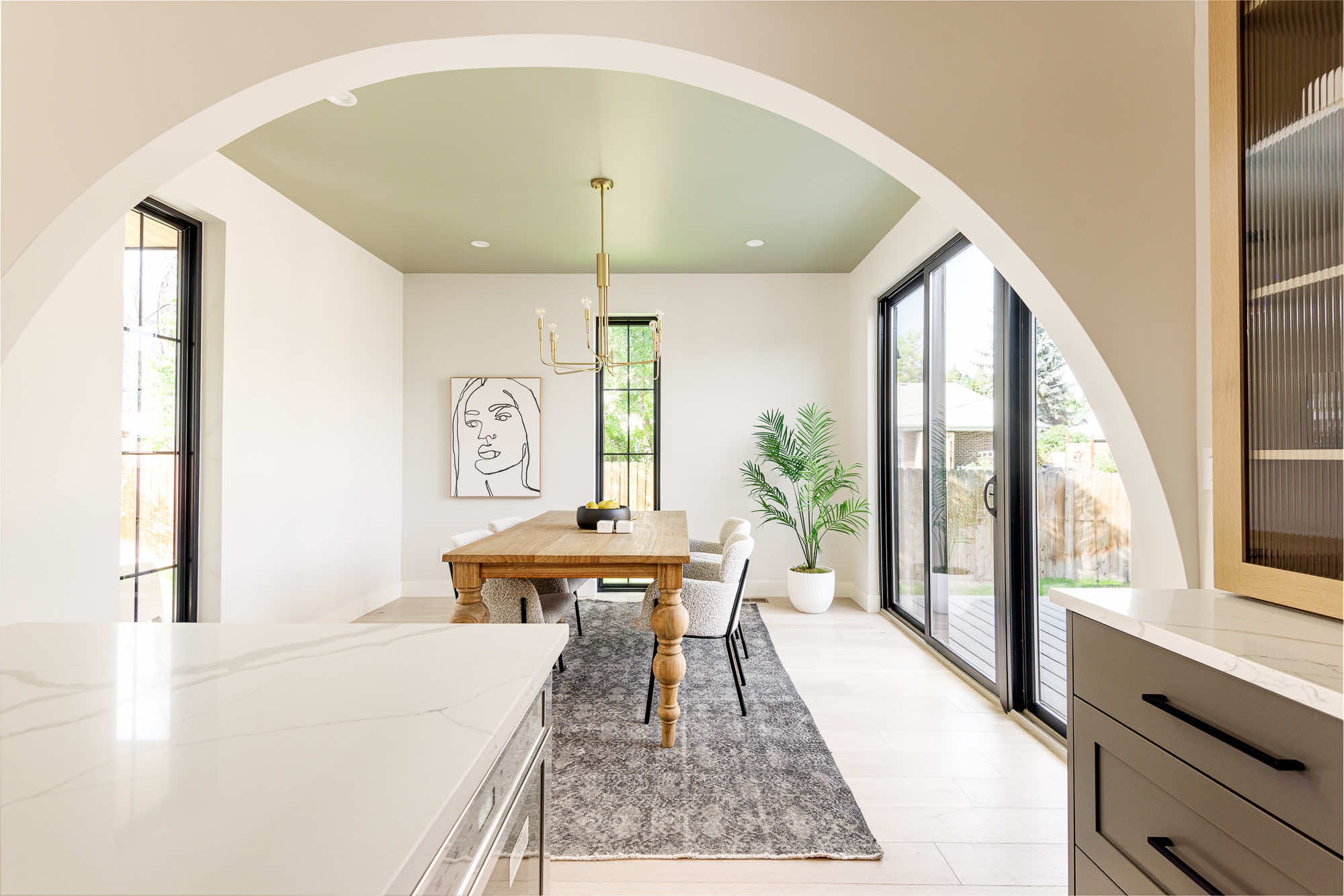 Dining room seen through a round arch, with a green ceiling, brass chandelier and a wood table