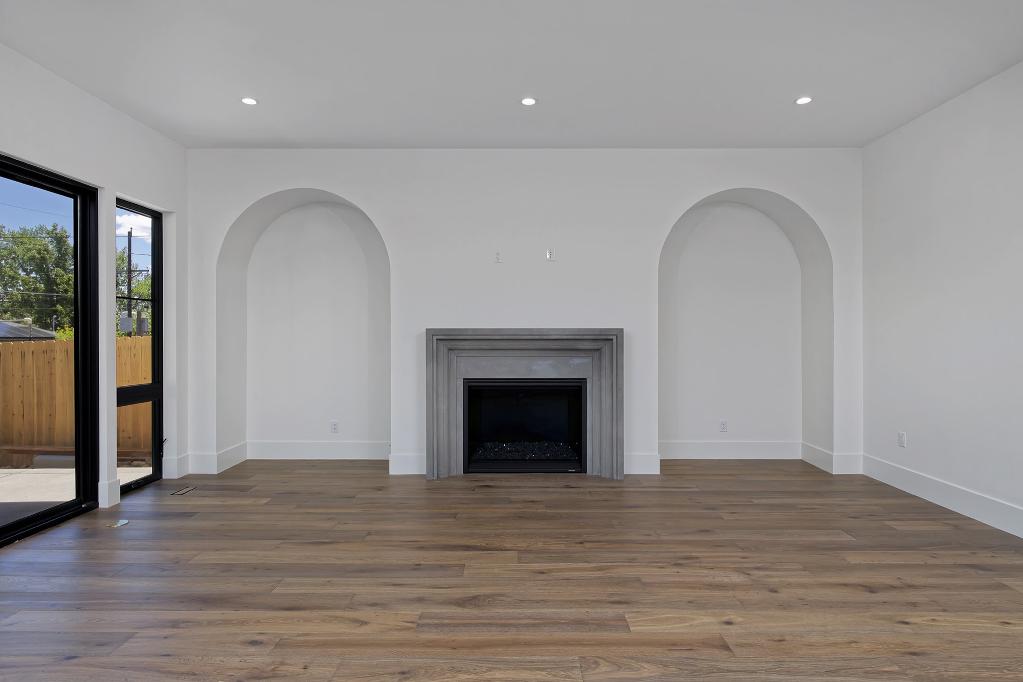 Gray fireplace between two arched niches on a white wall, with black-framed glass doors at the left