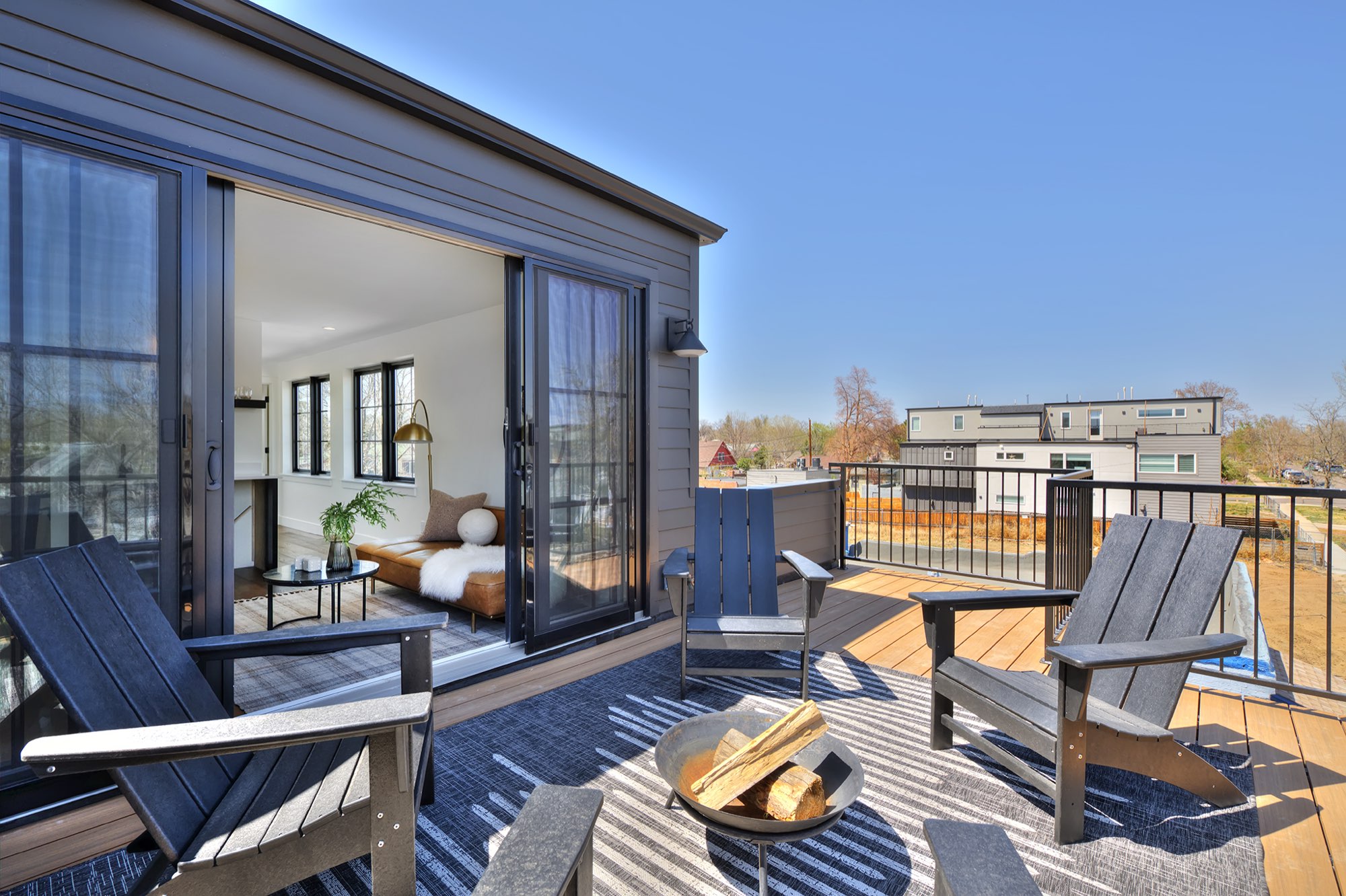 Rooftop deck with outdoor chairs and a fire bowl beside wide black-framed sliding doors to the lounge