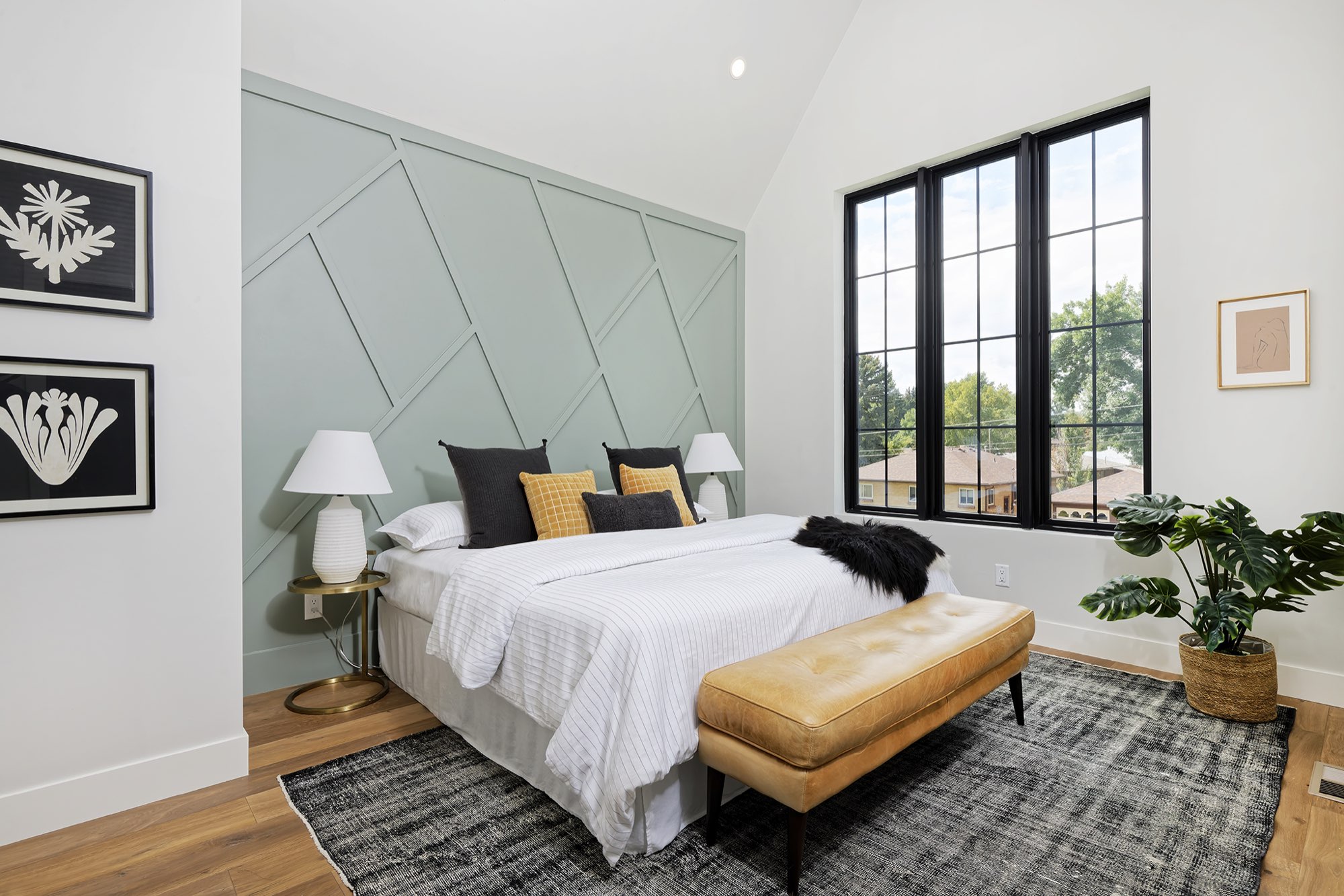 Primary bedroom with a sage green geometric paneled wall, black-framed windows, a vaulted ceiling and wood floors