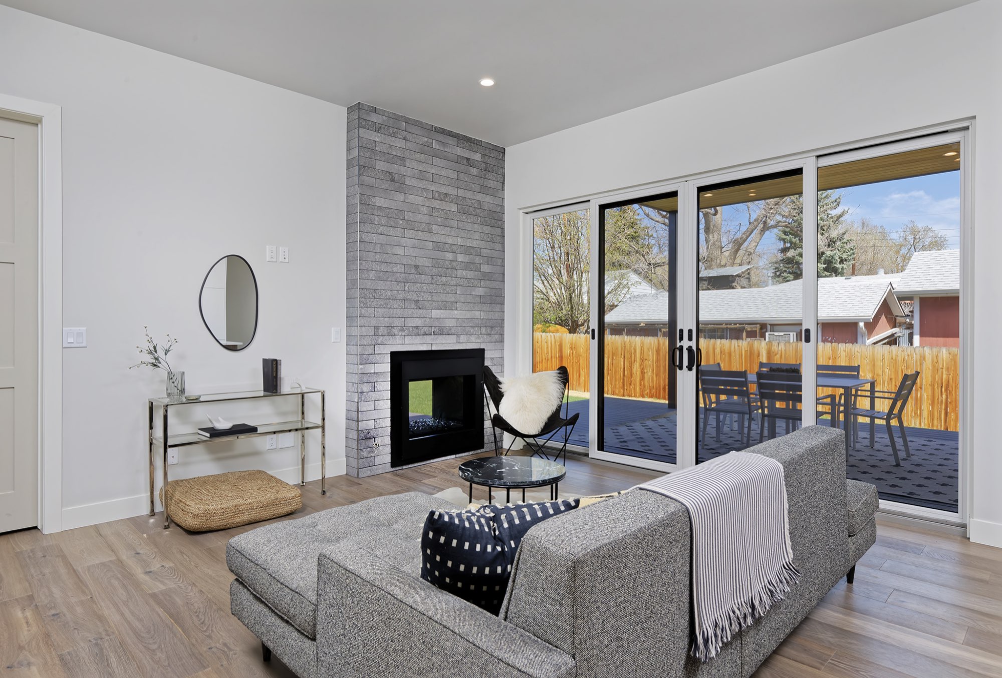 Living room with a fireplace in a gray stacked wall, wood-look floors and black-framed sliding doors to the covered deck