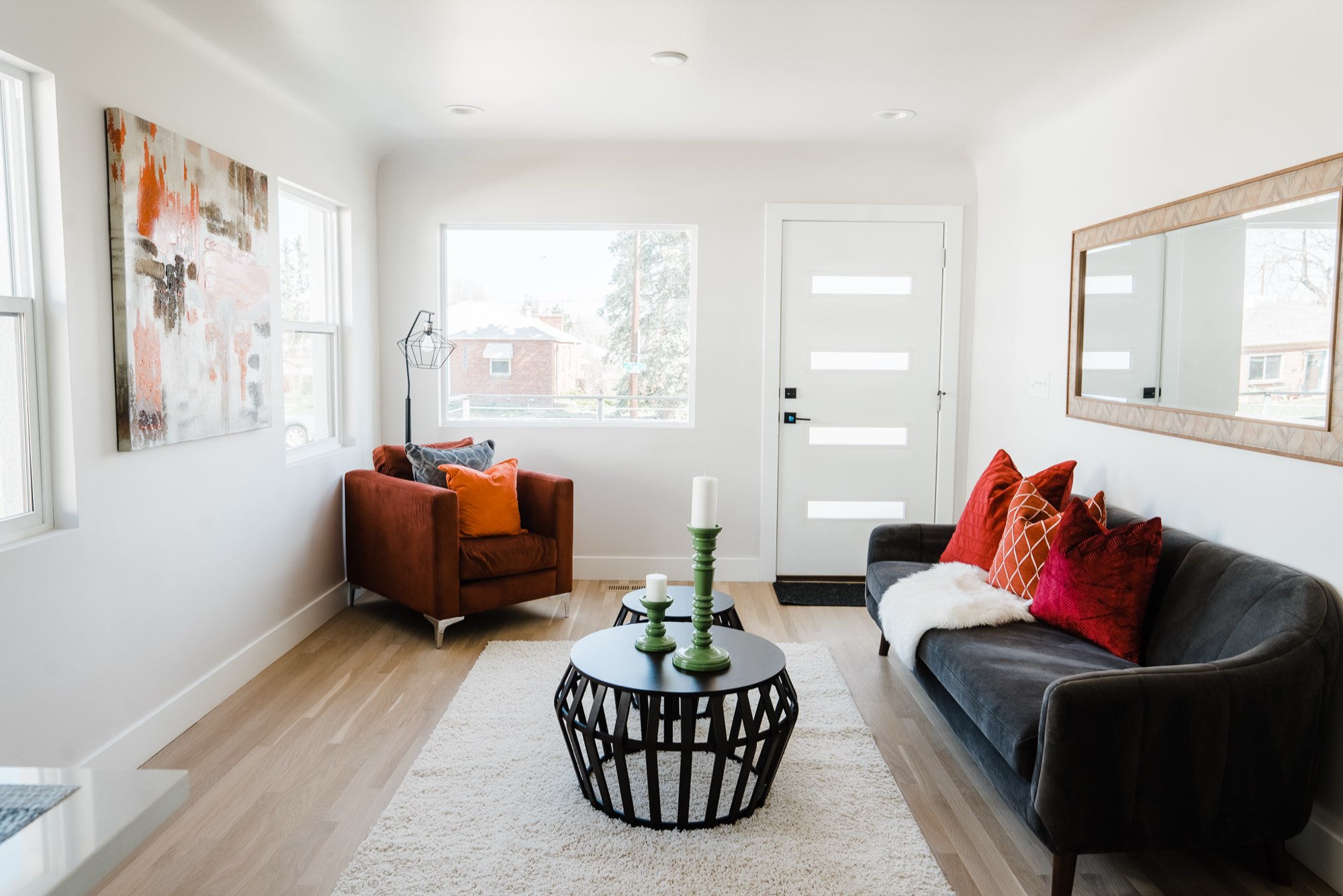 Living room with light wood floors, a gray sofa, a rust armchair, a large orange abstract painting and a white door with narrow windows