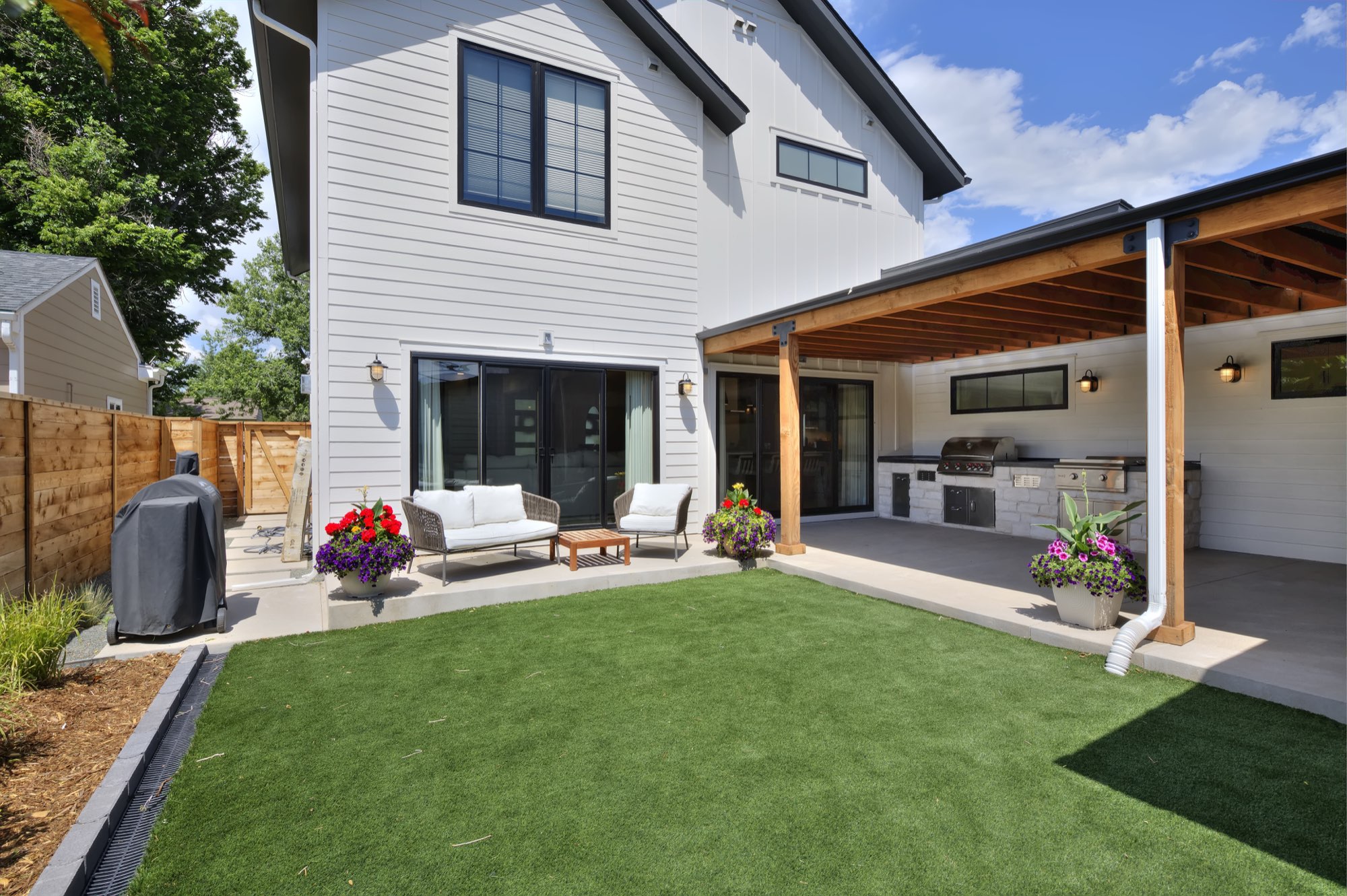 Backyard of the Denver custom home with a covered concrete patio, outdoor kitchen, sitting area and a lawn