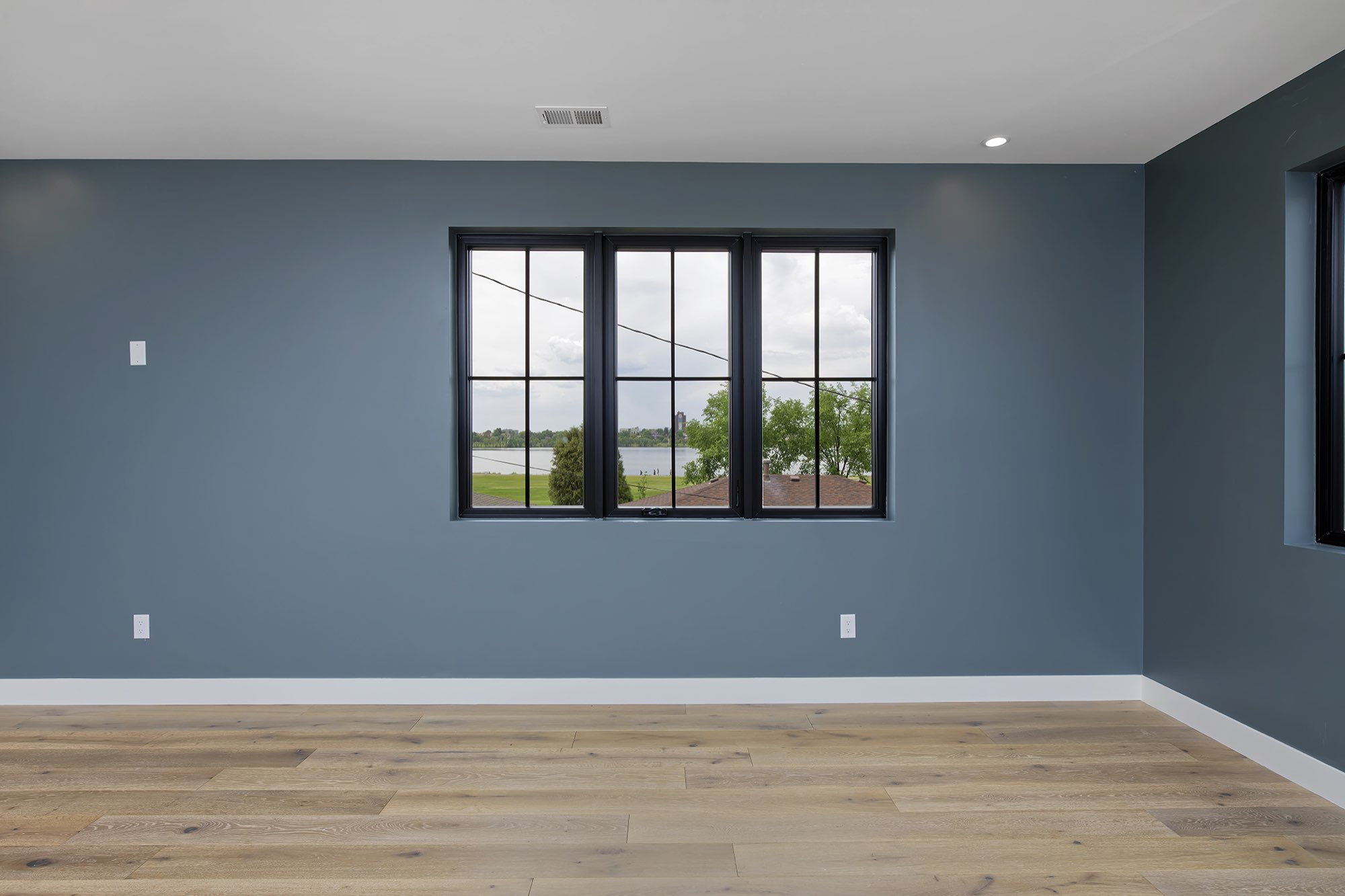 Black-framed bedroom windows with a view across the neighborhood to the lake