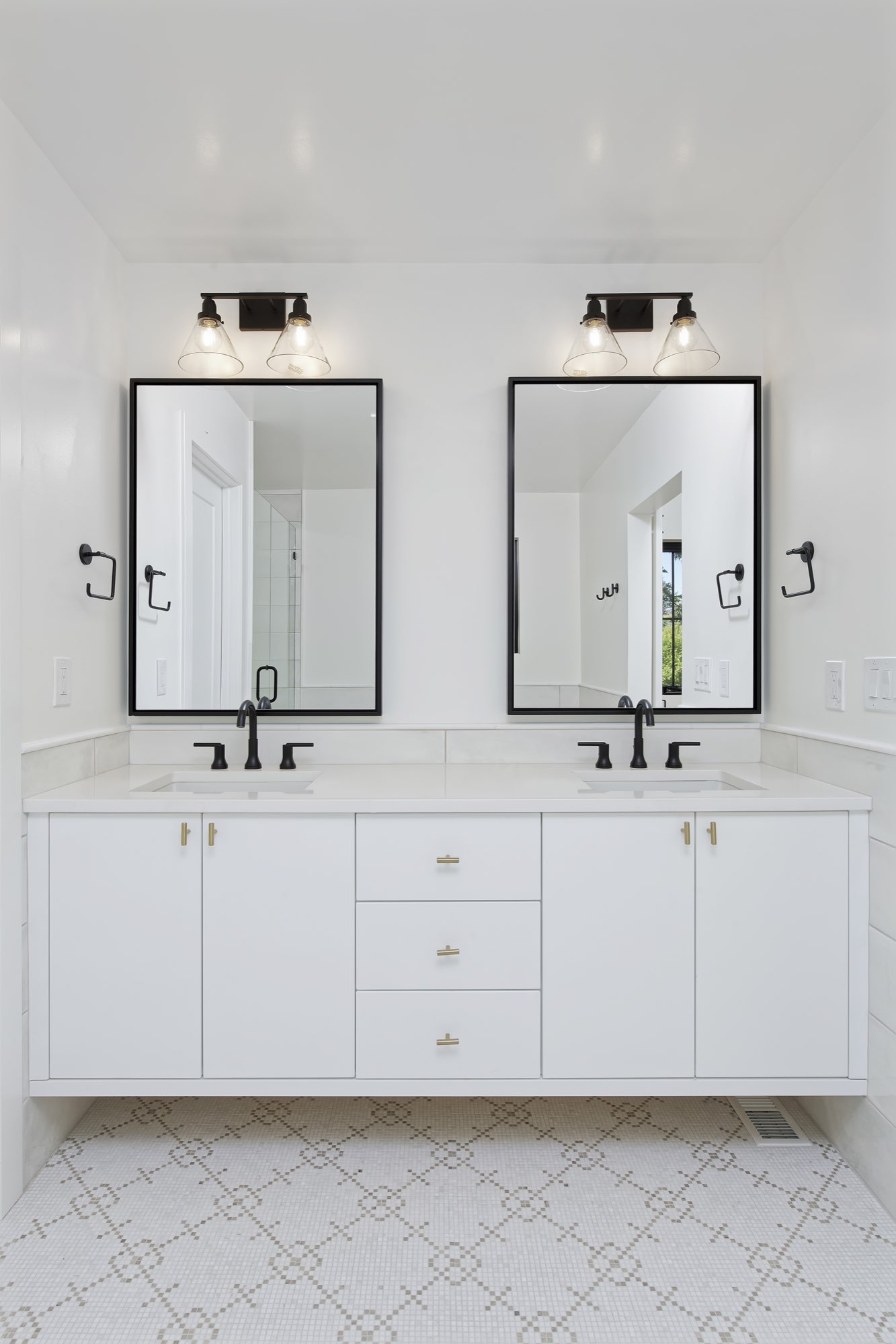 Floating white double vanity with two black-framed mirrors, black sconces and a patterned tile floor