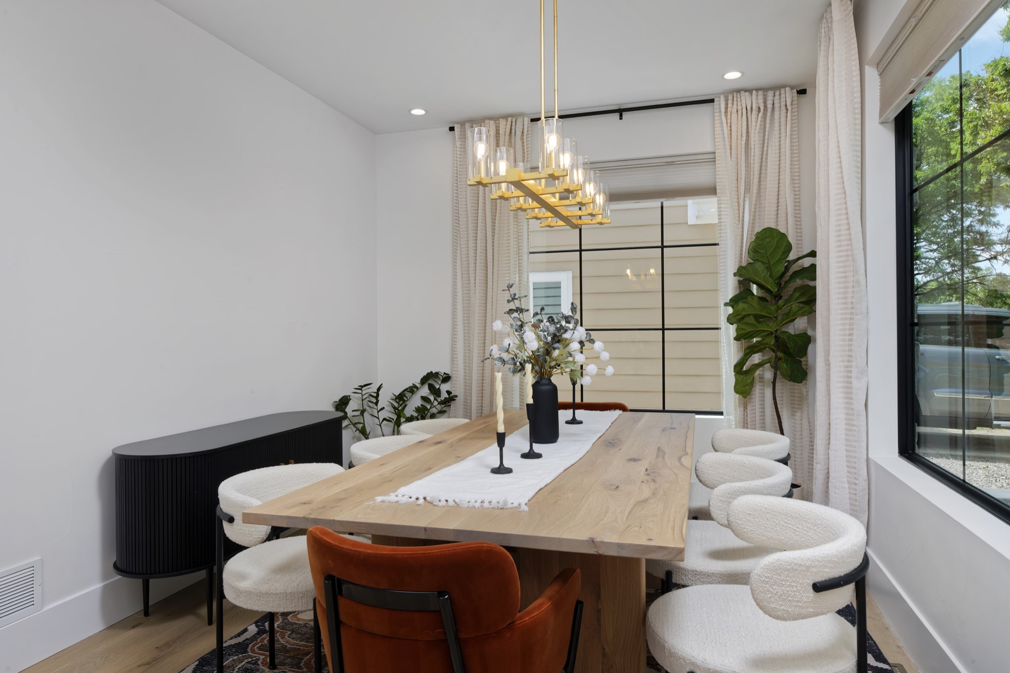 Dining room table with round upholstered chairs, a black cabinet and a brass chandelier