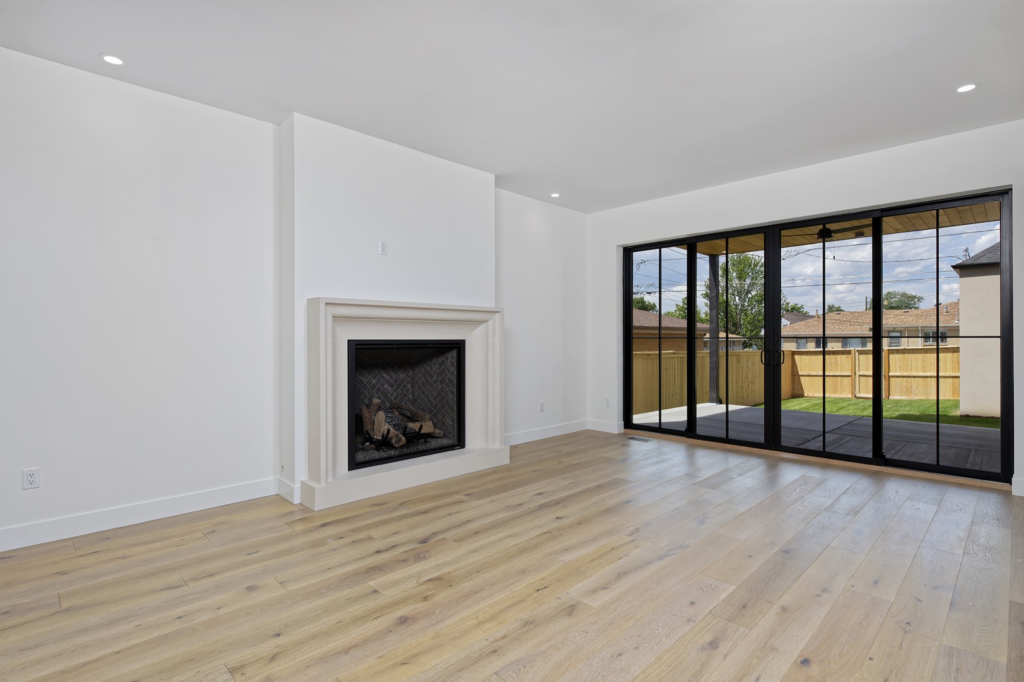 Living room with a pale fireplace, wide-plank light wood floors and a wall of black-framed sliding doors to the patio