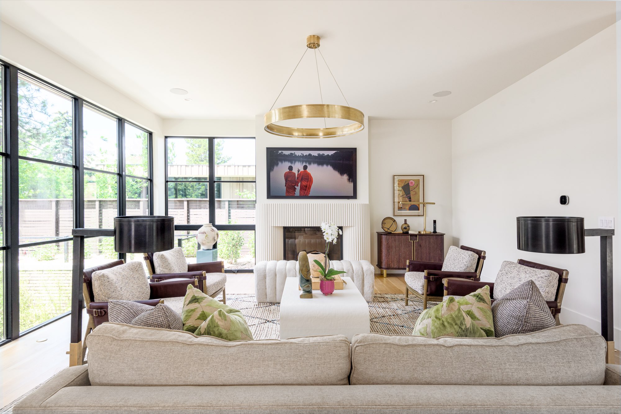 Living room with a fireplace, a brass ring chandelier, black-framed windows and light wood floors