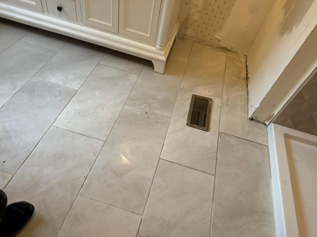 Cream large format vinyl tile flooring finished around a floor vent and cabinet base in a mobile home