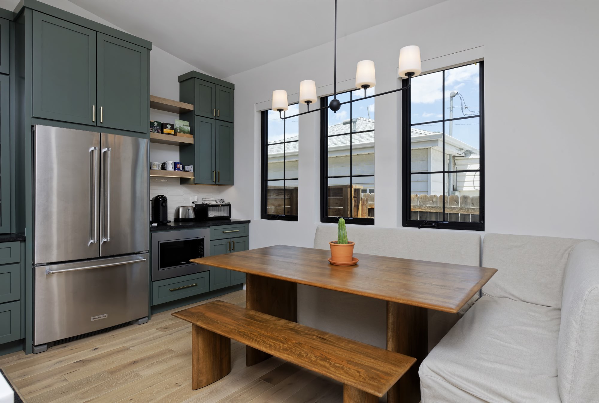 Breakfast nook with a wood table, built-in bench and three black-framed windows under a chandelier