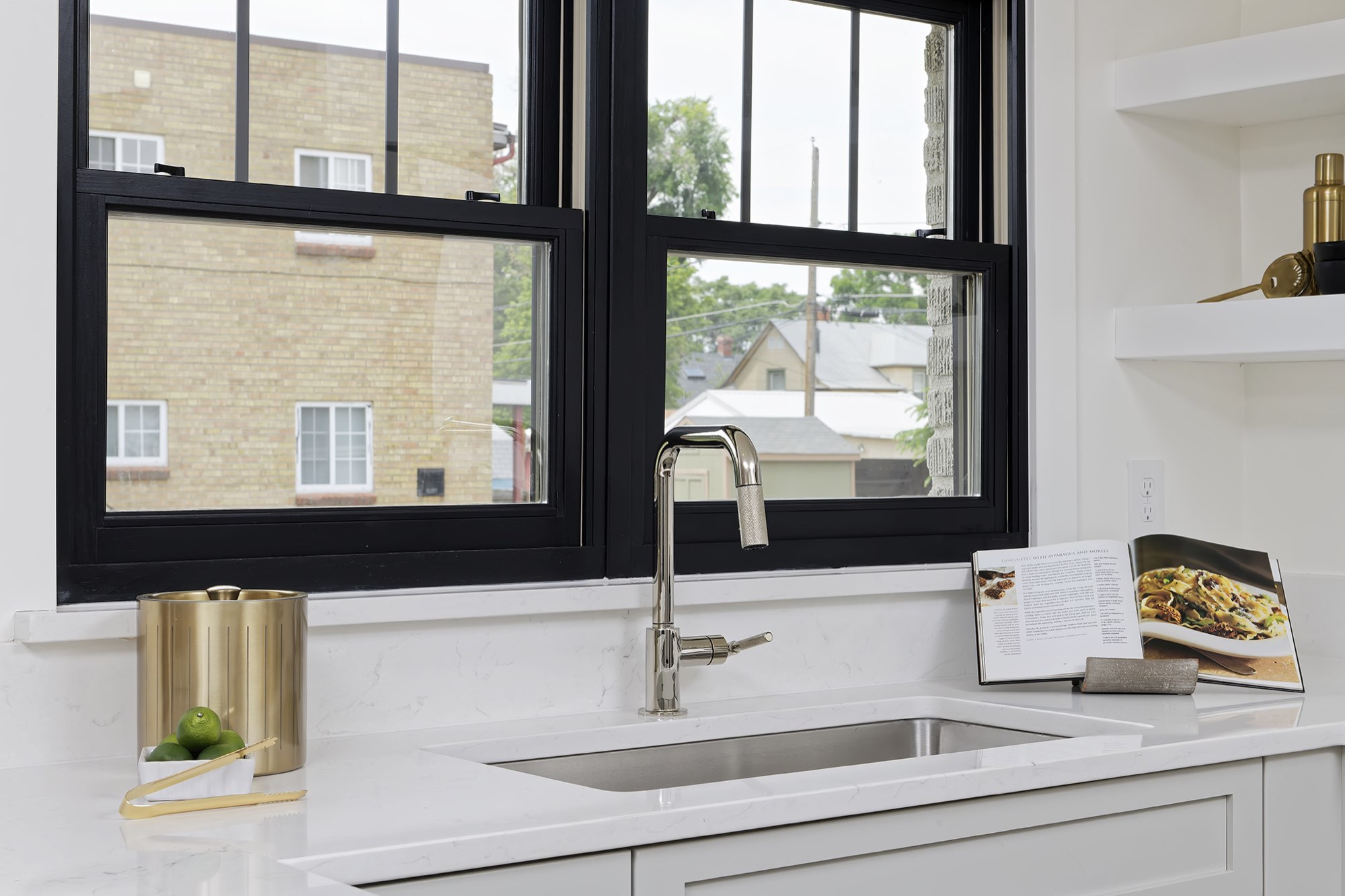 Stainless faucet over the kitchen sink in front of a black-framed double-hung window