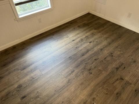 Finished dark wood-look luxury vinyl plank flooring running to fresh white baseboard in a mobile home