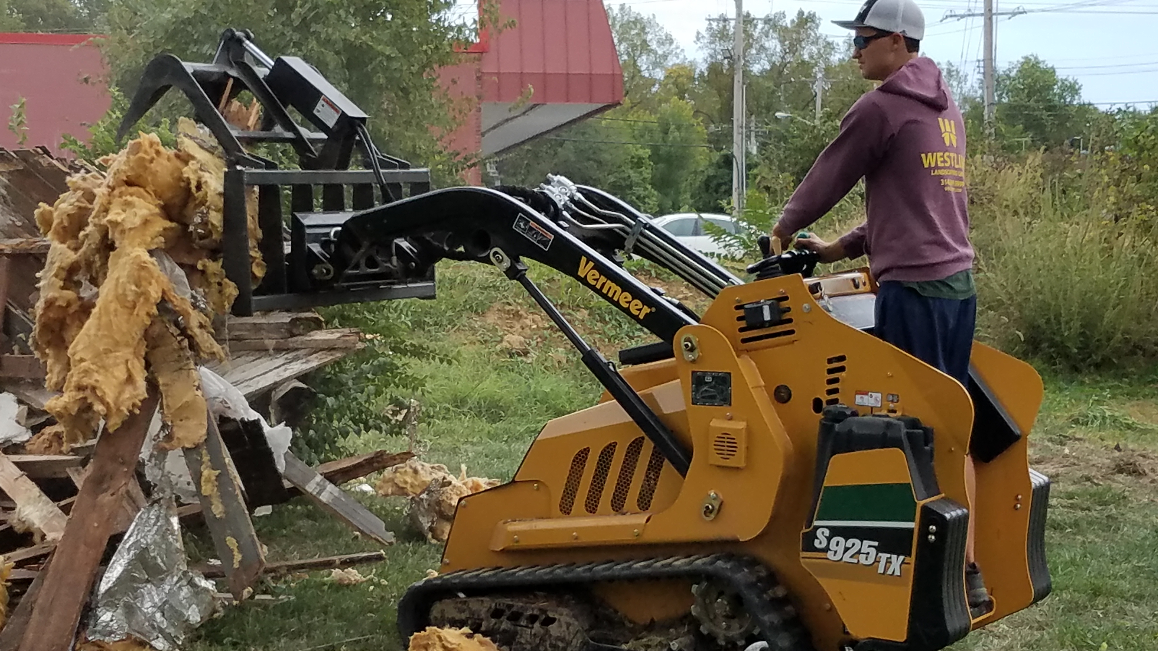 Compact track loader clearing stump grindings and debris