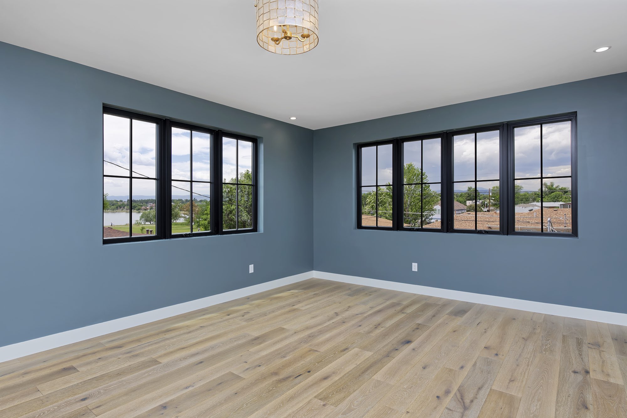 Primary bedroom with slate blue walls, black-framed windows and wide-plank light wood floors