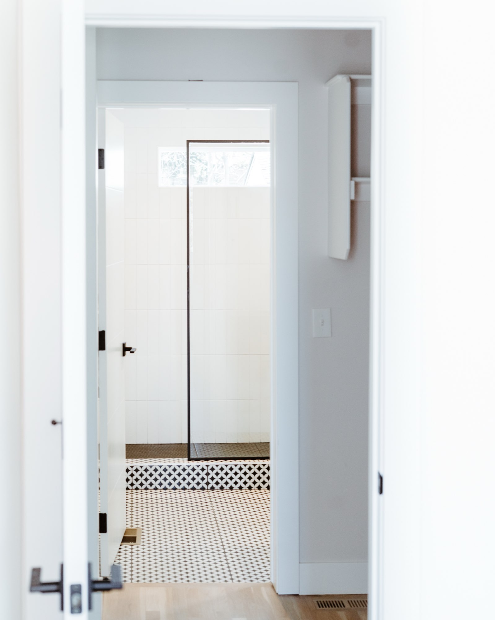 Hallway door opening to a bathroom with a black and white patterned tile floor and a glass shower