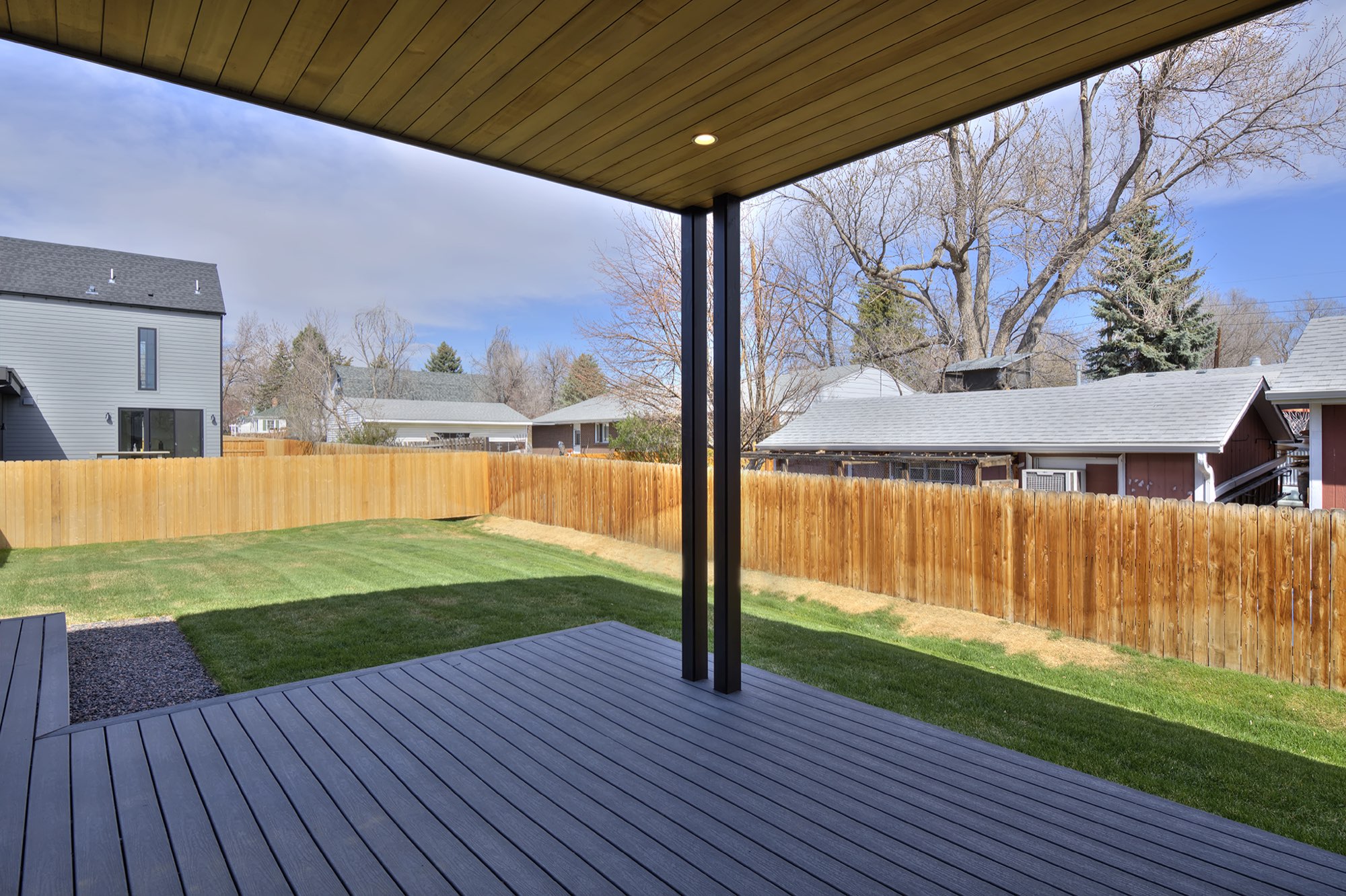 Covered deck under a wood-plank ceiling with recessed lights, a composite deck floor and a fenced yard