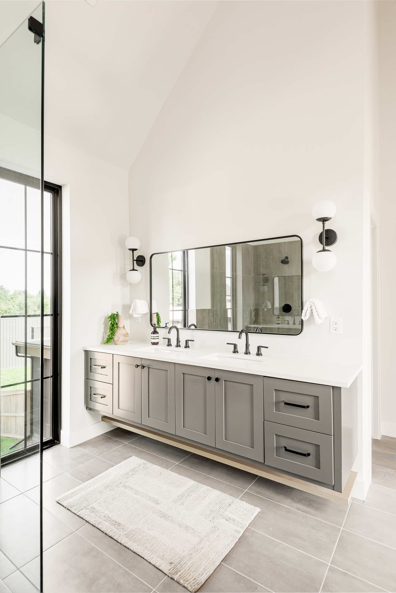 Primary bathroom floating gray vanity with a black framed mirror and globe sconces