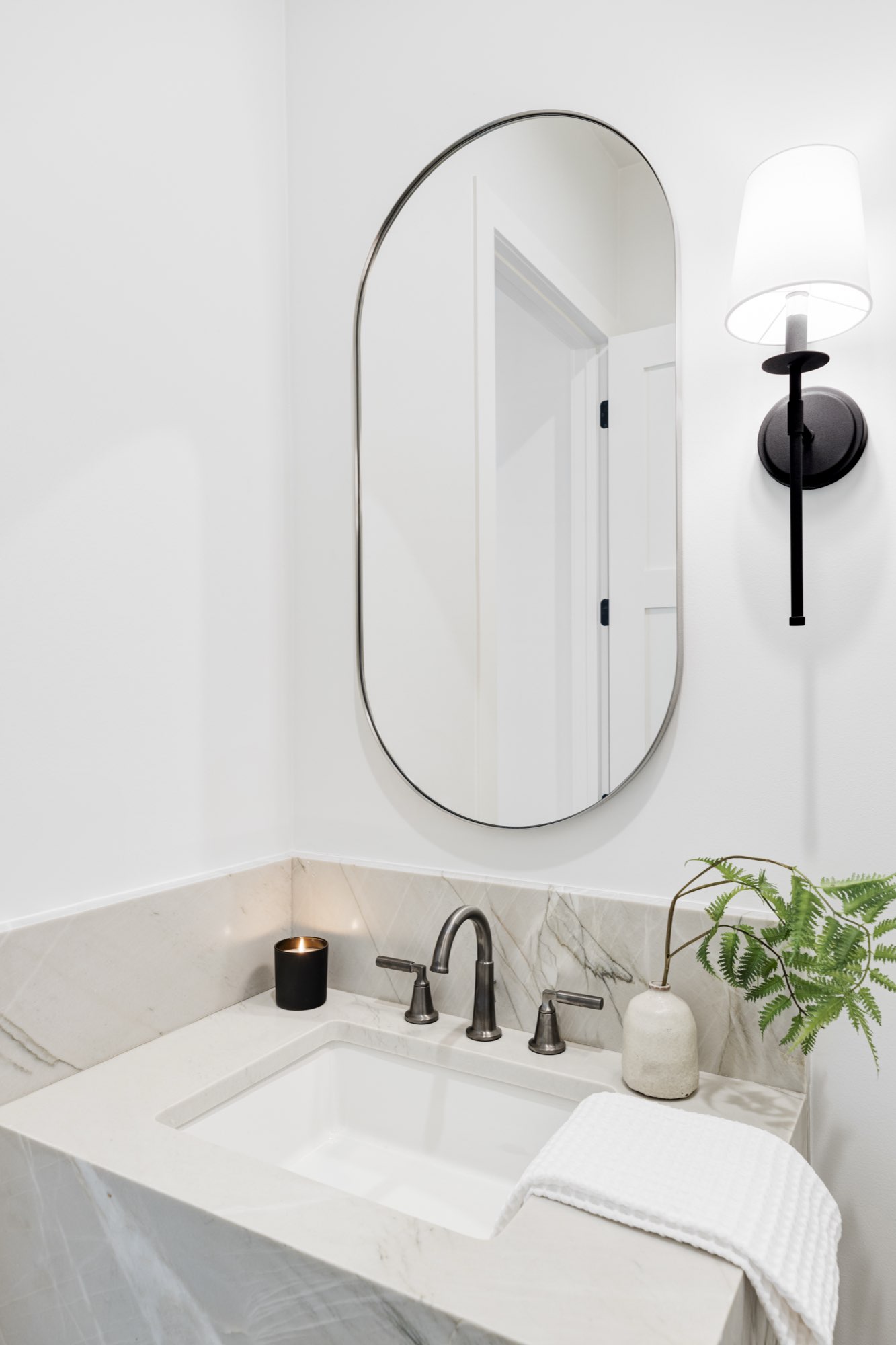 Powder room with an oval mirror, a black sconce and a stone-look floating vanity