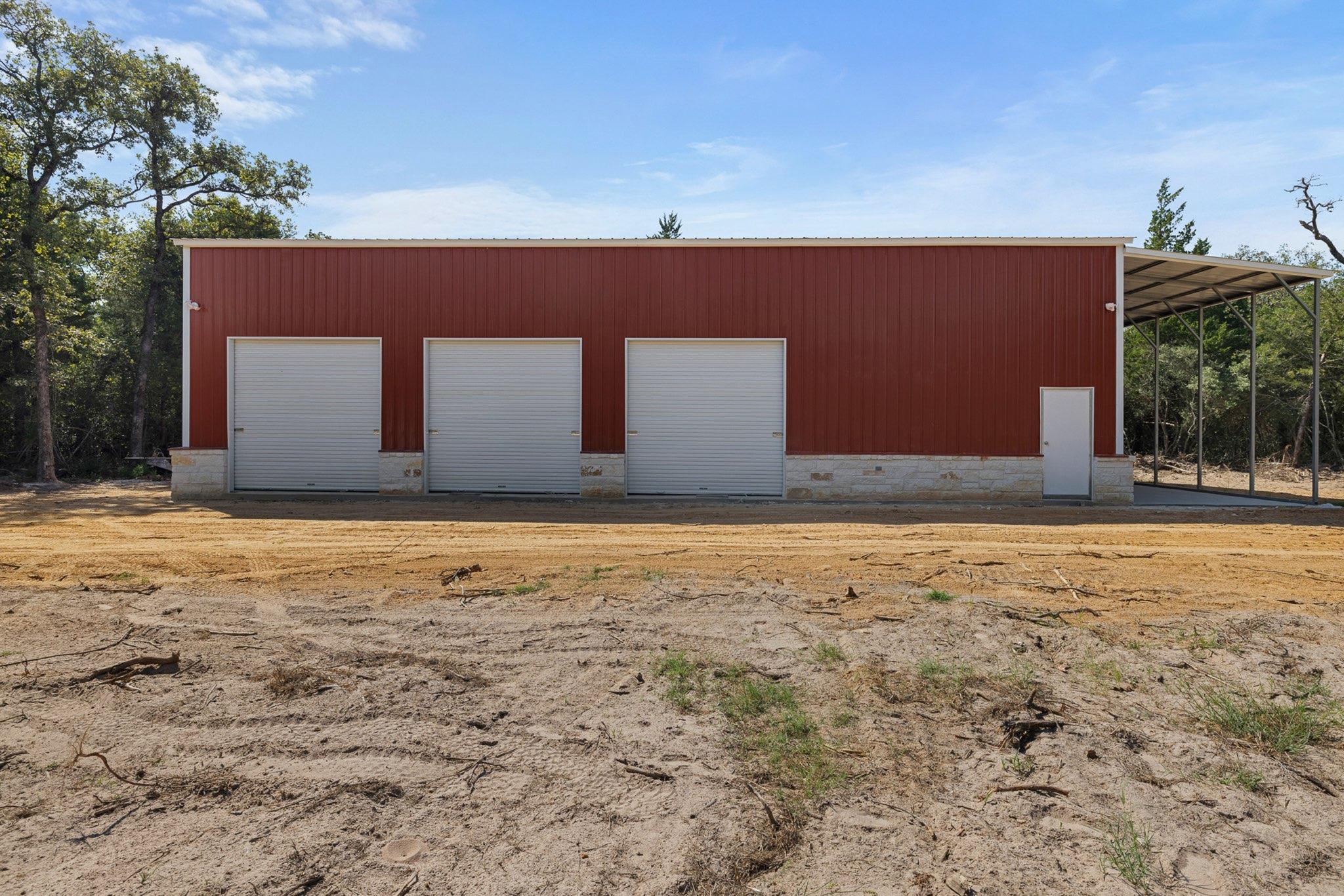 Red metal shop building with three roll-up doors on a cleared Texas lot