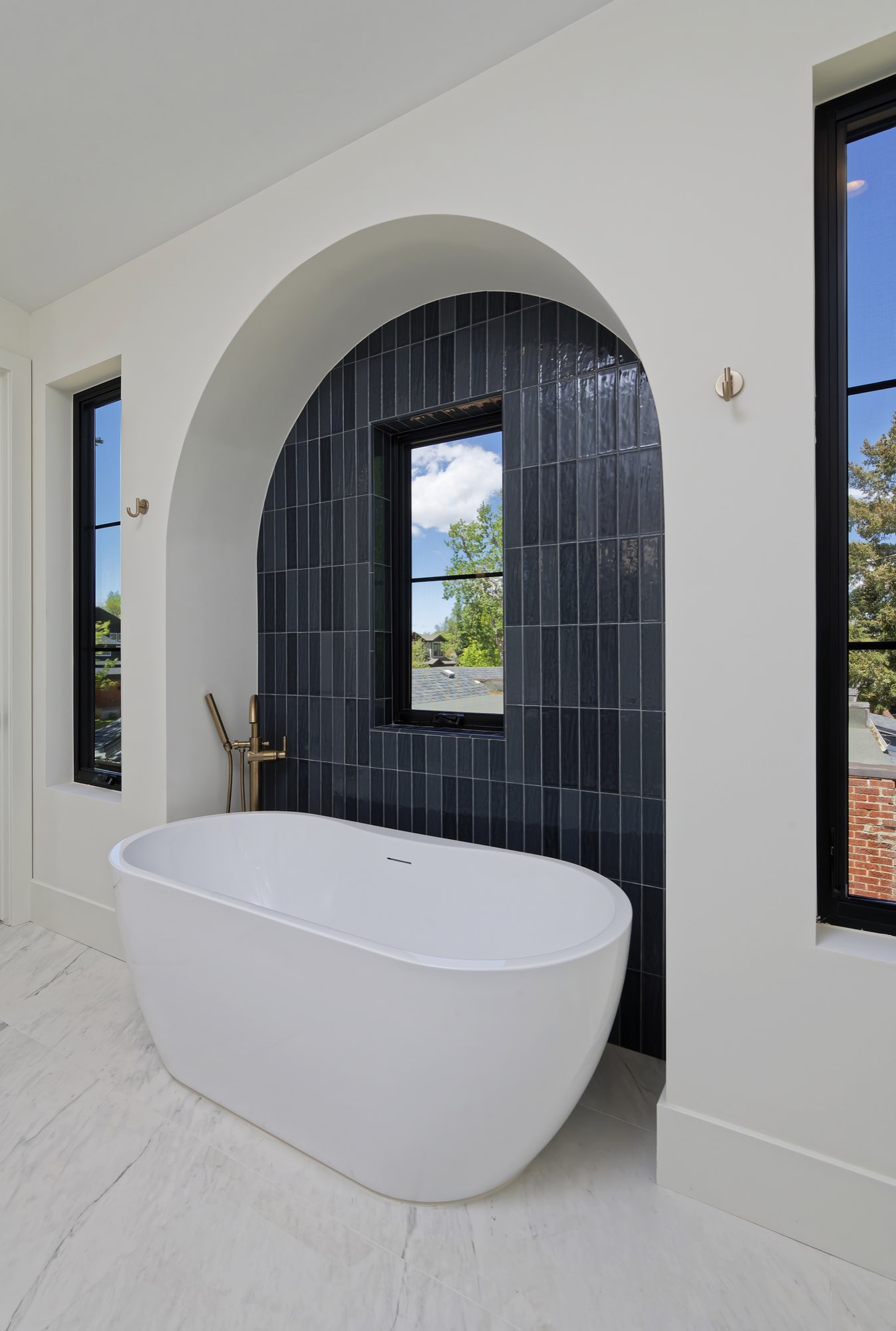 Freestanding white tub in an arched niche of blue tile with a black-framed window