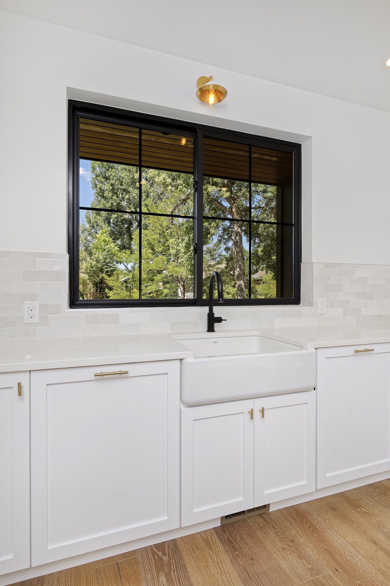 Farmhouse sink with a black faucet under a black-framed window and a brass sconce