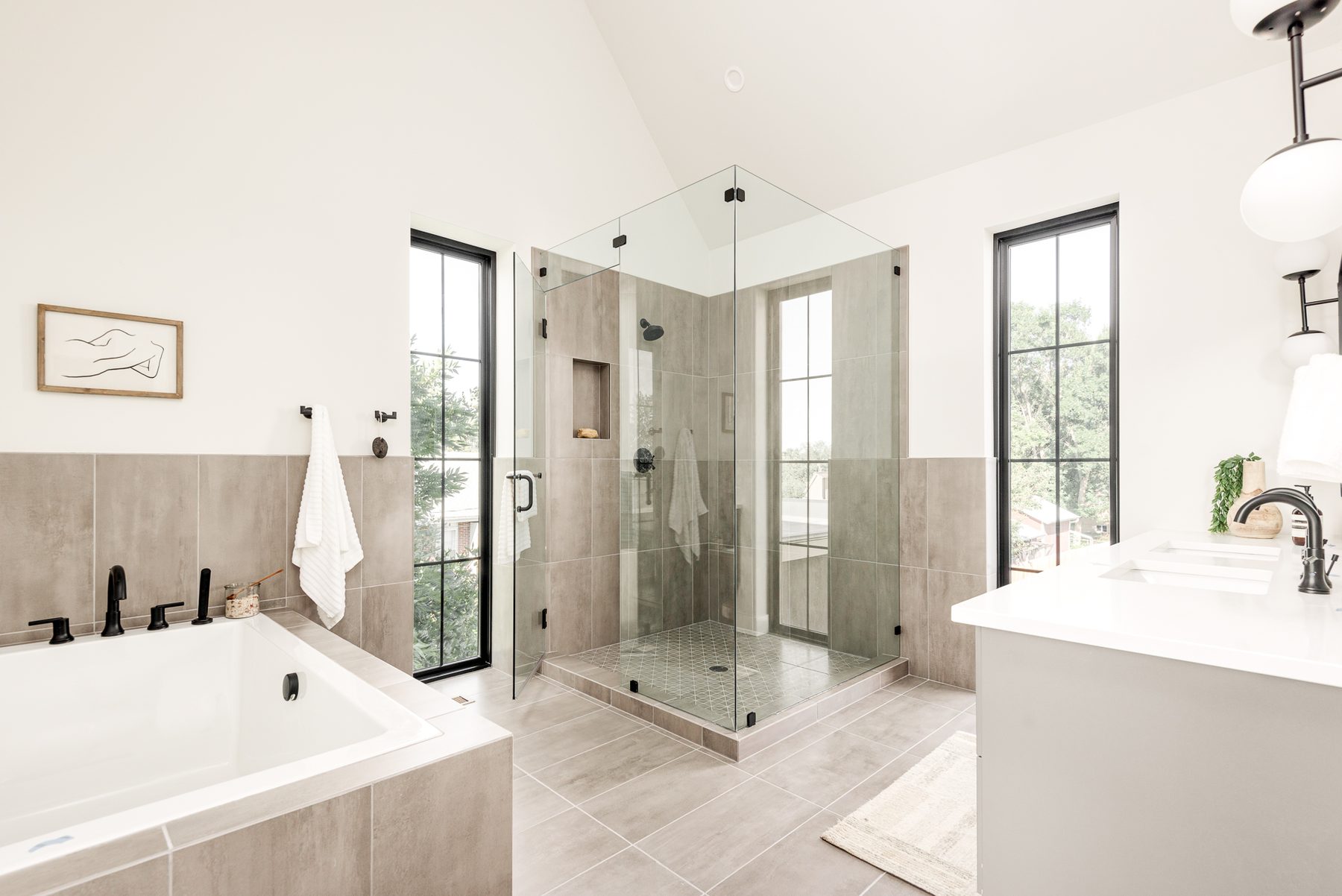 Primary bathroom with a vaulted ceiling, glass corner shower, soaking tub and tall black-framed windows
