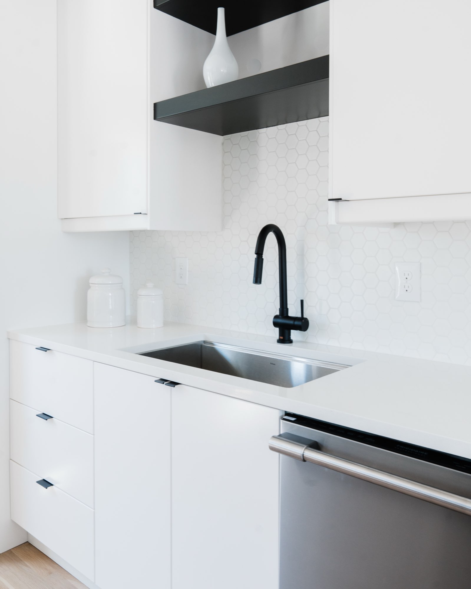 White cabinets, a dark floating shelf, a matte black pull-down faucet and white hex tile backsplash