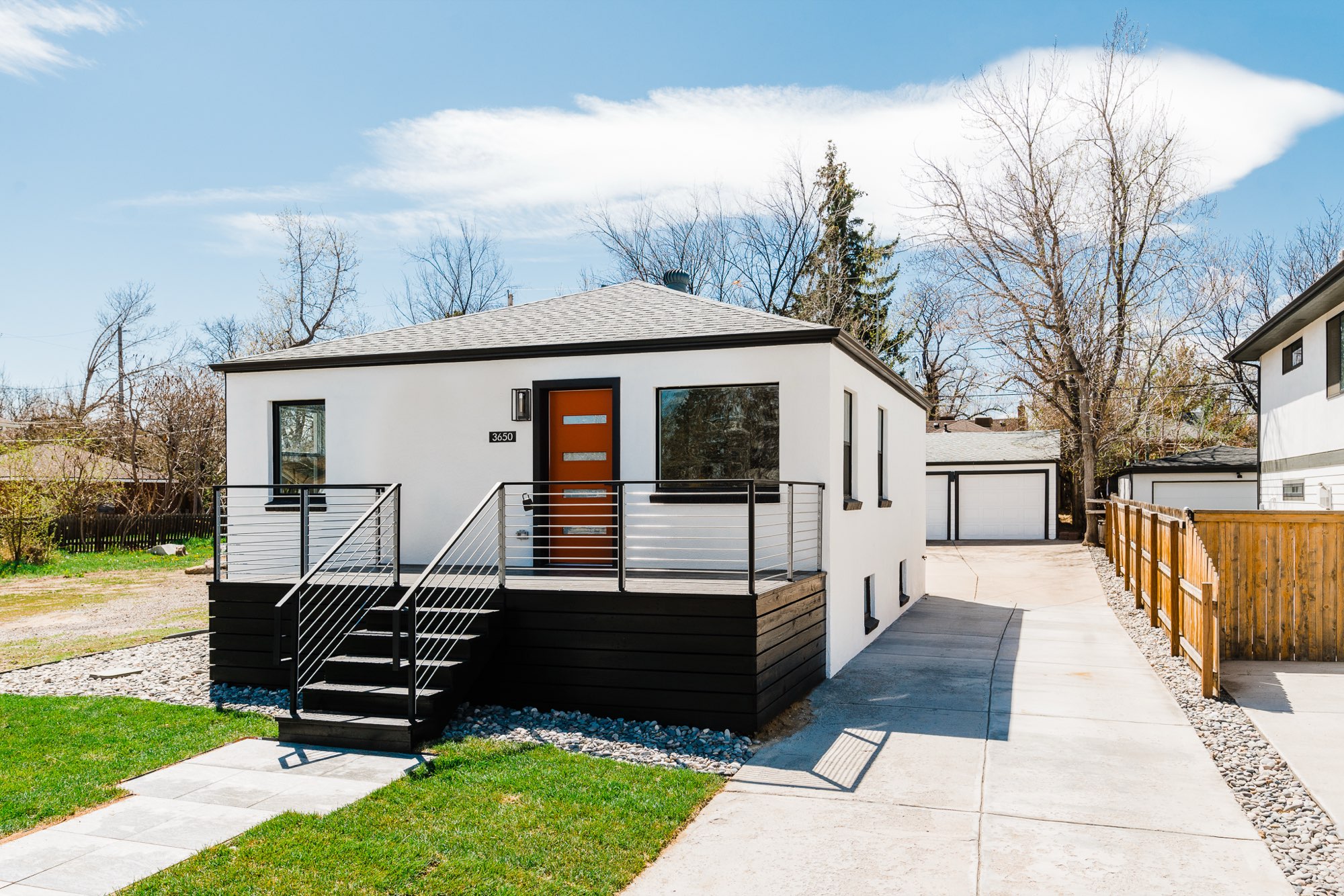 Front of the bungalow from the driveway side, with the deck stairs, a long concrete drive and a detached garage behind
