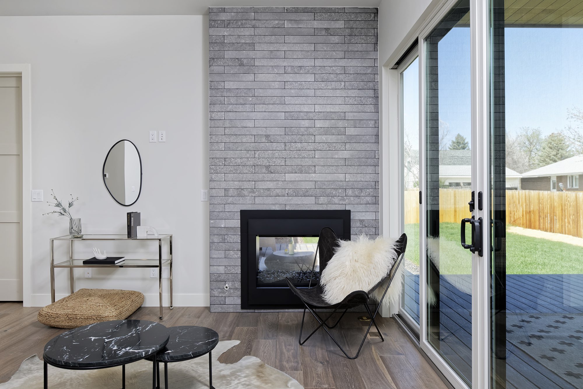 Fireplace wall beside black-framed sliders with a view of the deck and lawn