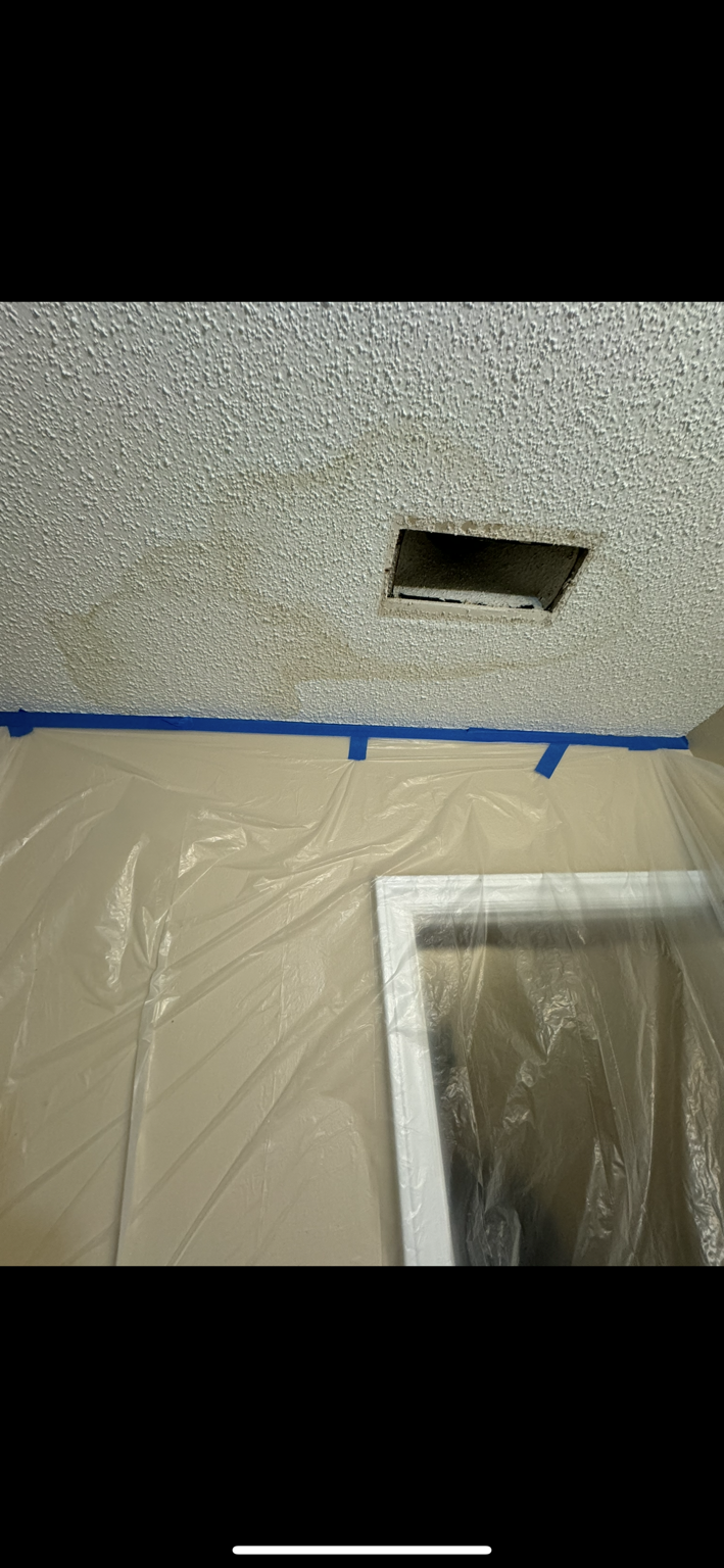 Water stained interior ceiling around a vent with the room masked off before leak repair